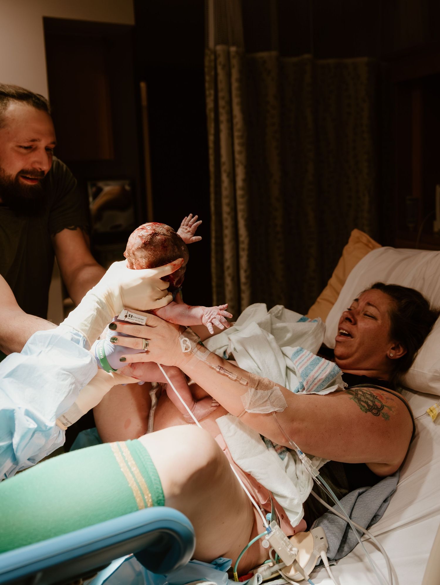 A joyful moment captured during childbirth as a newborn baby reaches out while being held in the delivery room.