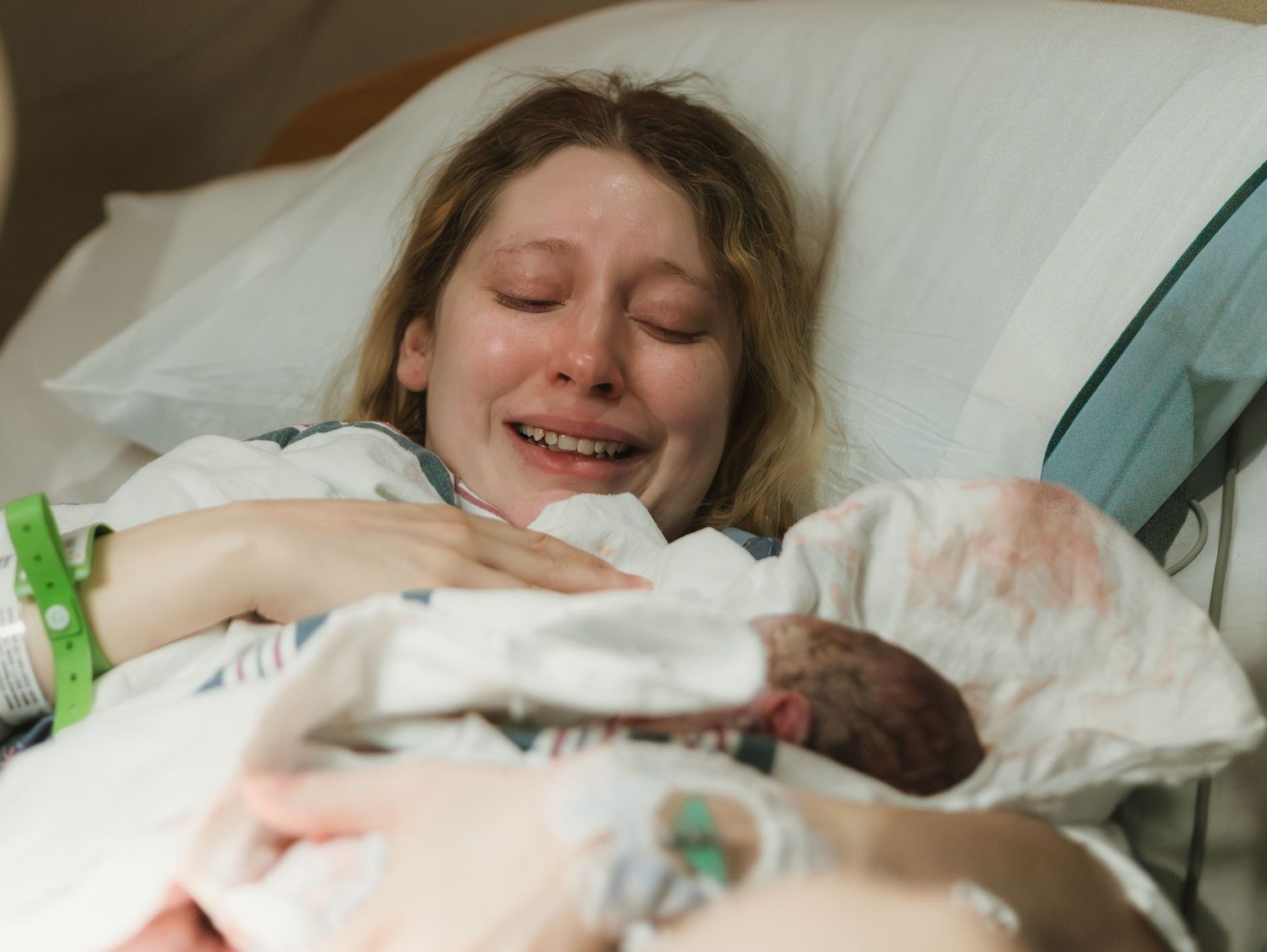 Emotional new mother crying tears of joy while holding her newborn baby in a hospital bed after delivery.