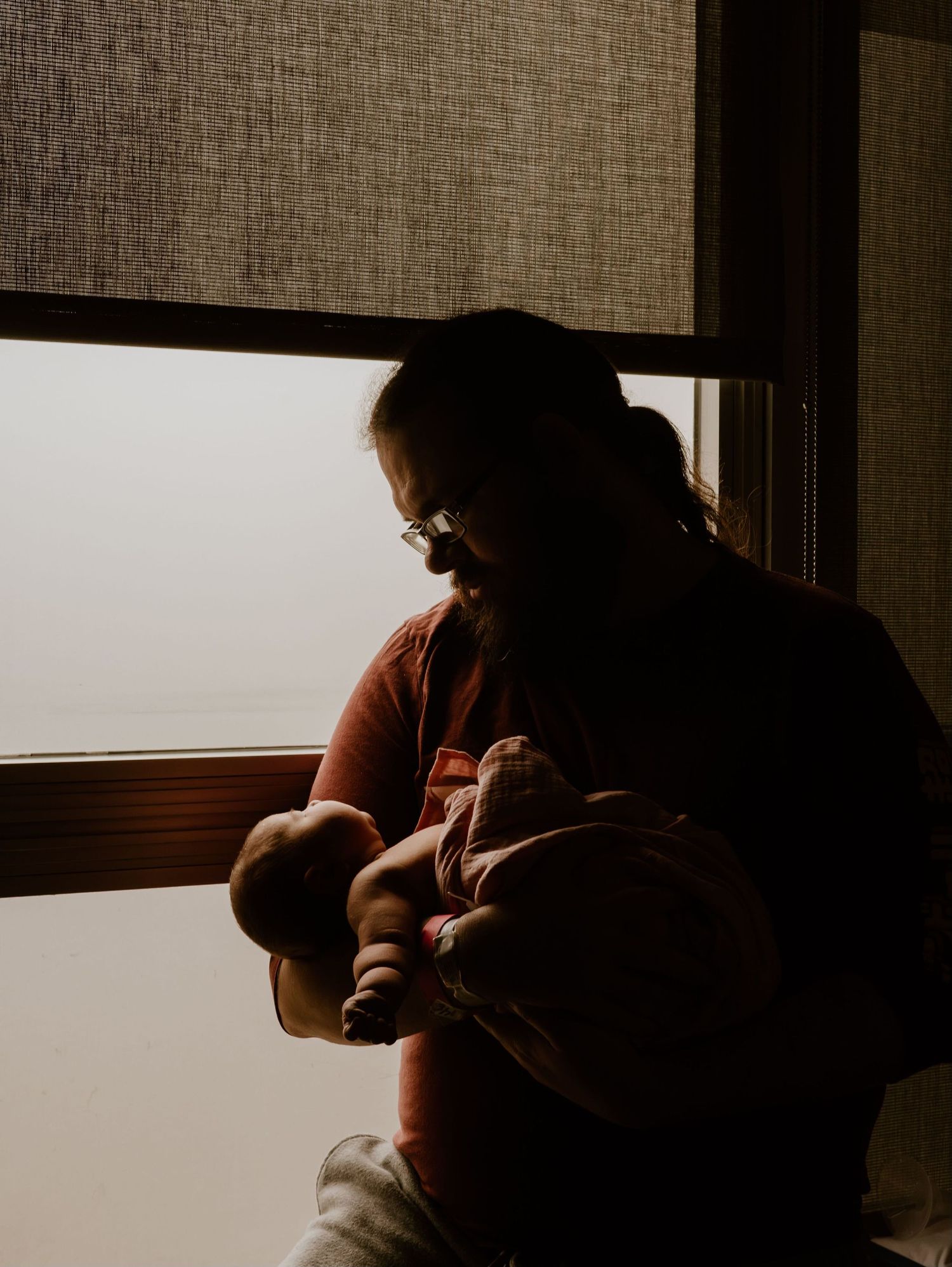 Silhouette of caregiver cradling newborn baby by window in warm lighting.