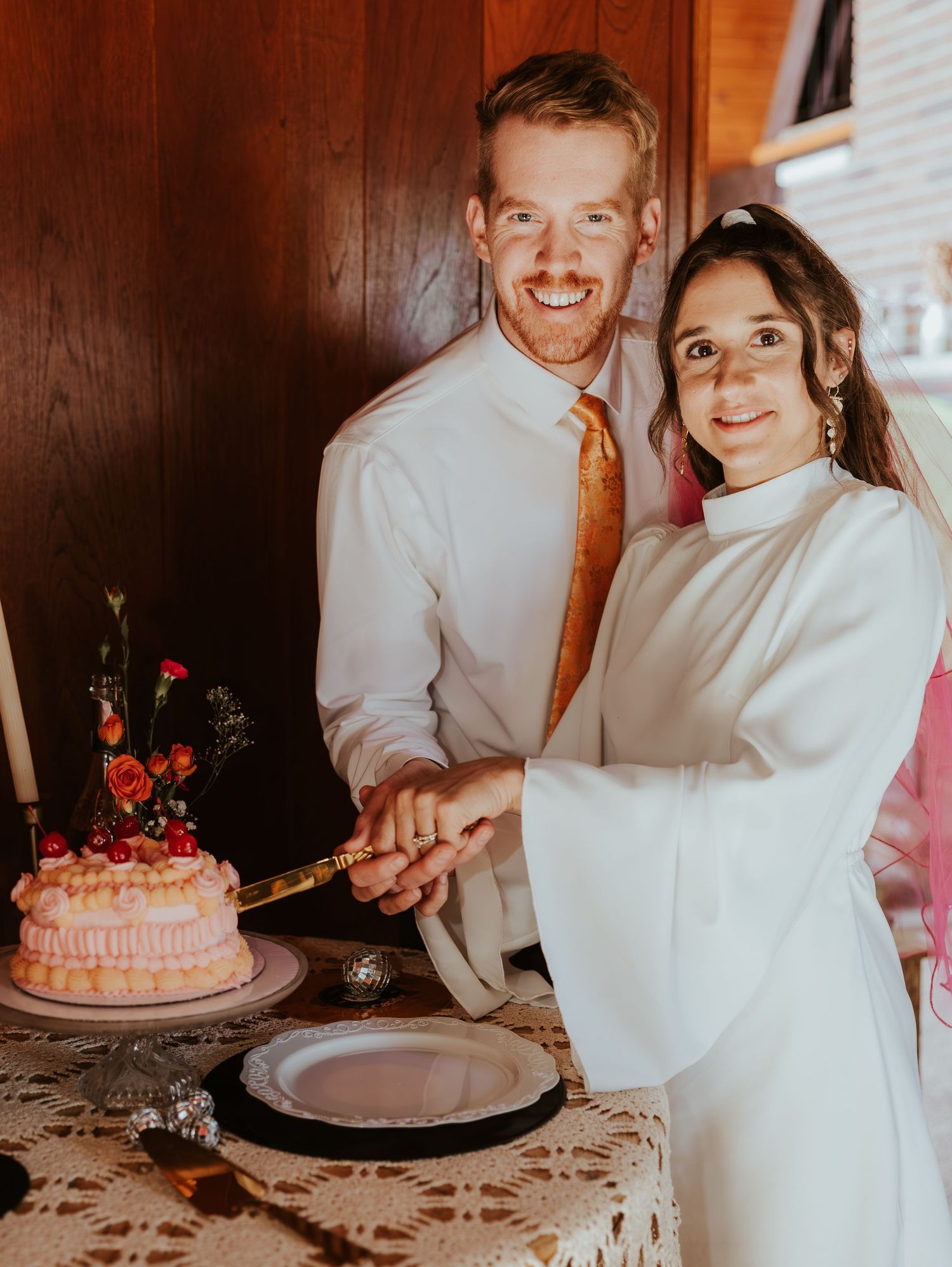 Newlyweds cutting their pink wedding cake together at reception table.