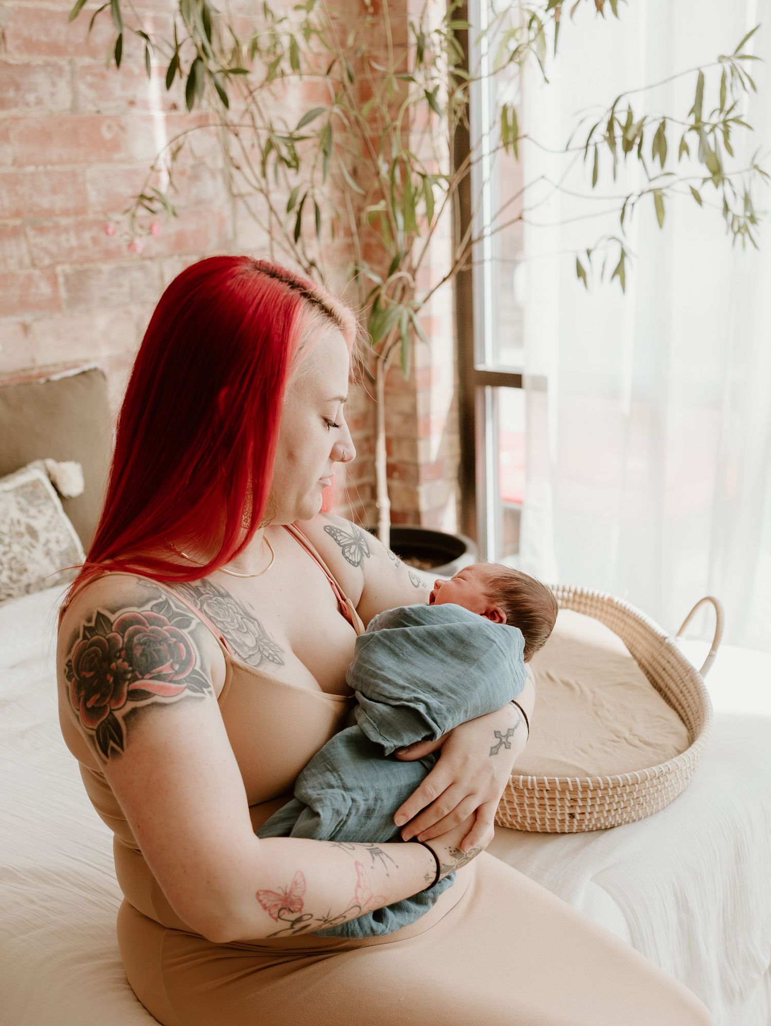 A tender moment of parent and newborn bonding on a couch with soft natural lighting and willow branches in the background.