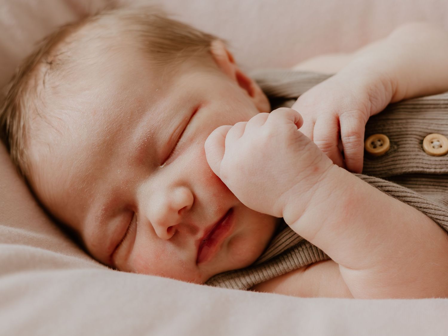 A sleeping newborn baby lies peacefully in a cozy blanket with soft natural lighting.