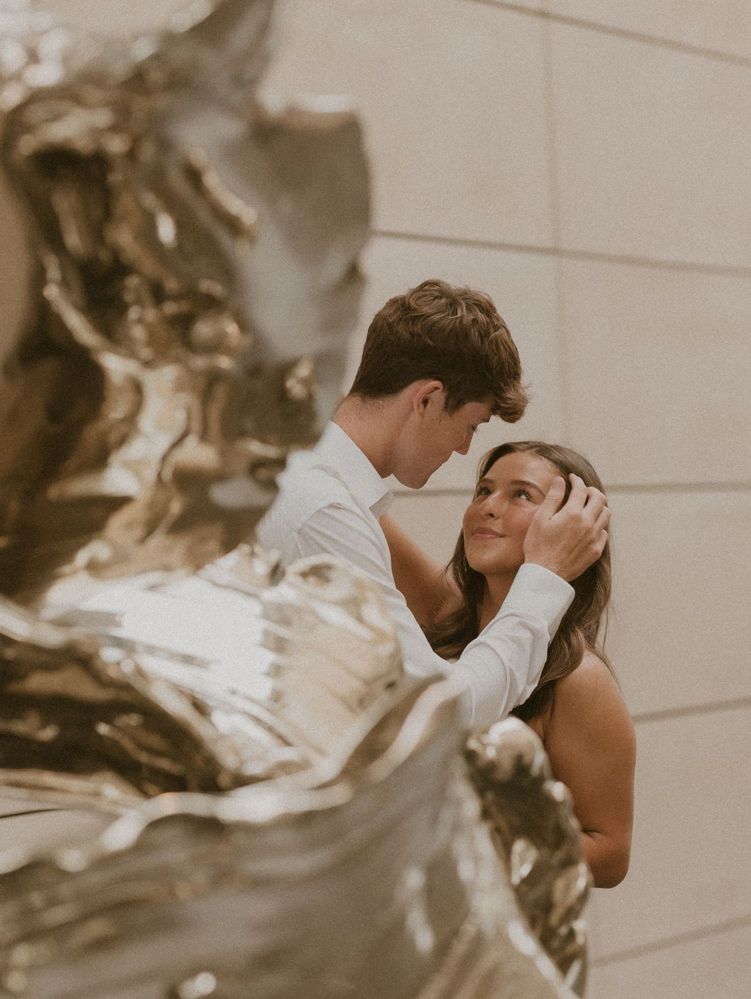 An intimate moment captured in sepia tones with sculptural elements in background.