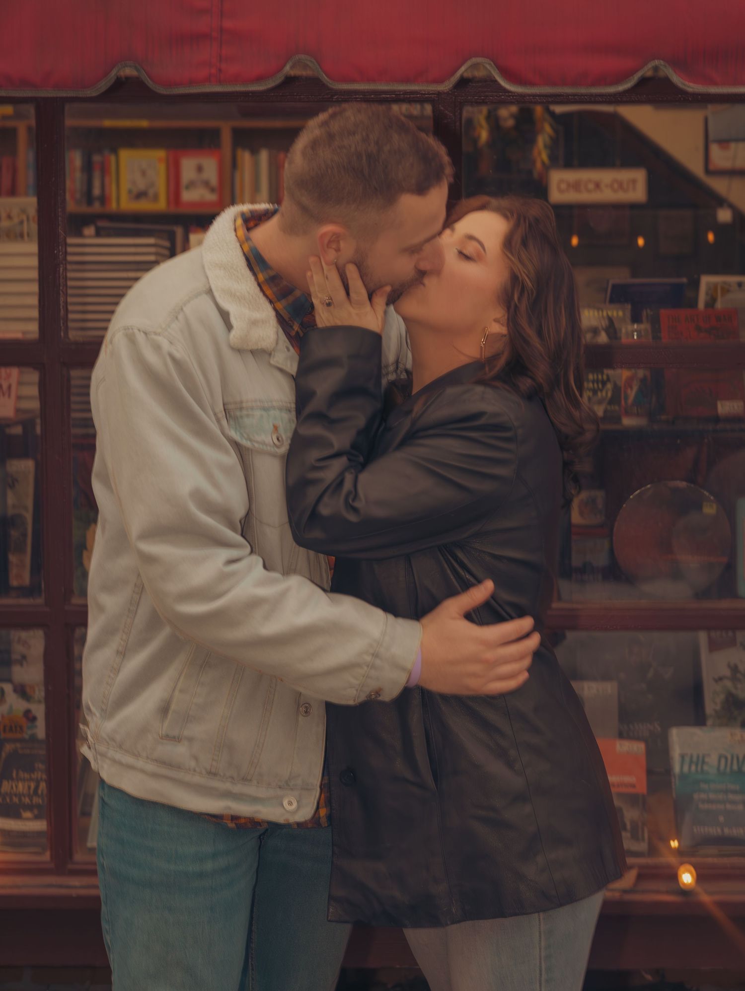 A couple shares an intimate moment outside a storefront with red awning at night.