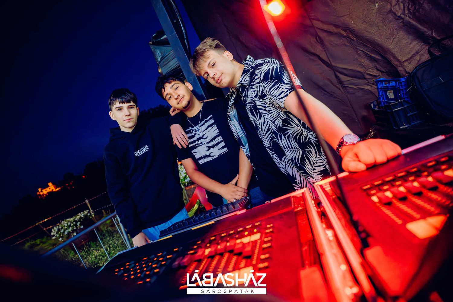 DJ performs at a nightclub with red and blue lighting creating an atmospheric electronic music environment.