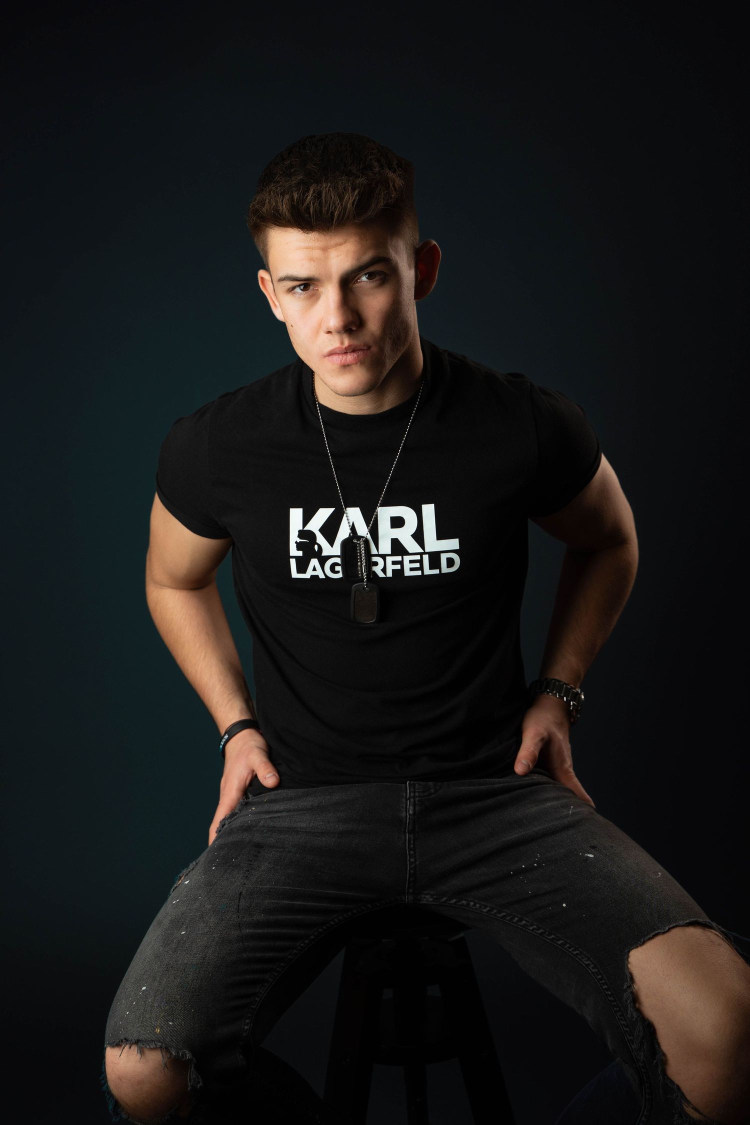 Athletic model in Karl Lagerfeld shirt posing on chair with dramatic lighting.