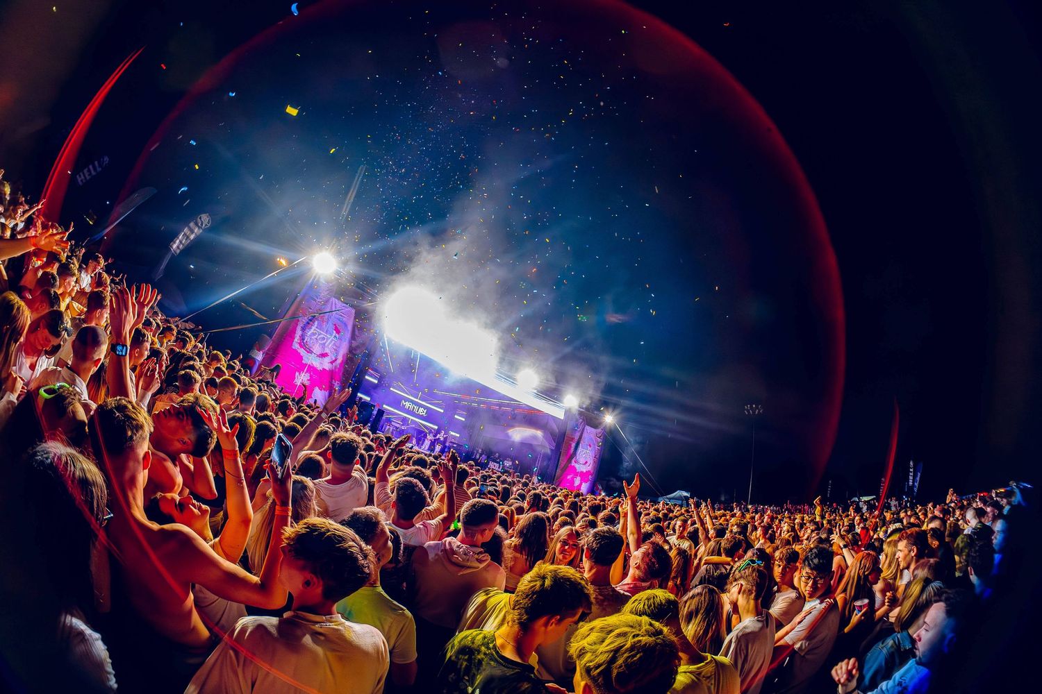 Colorful concert lights illuminate a large crowd of festival-goers during a nighttime music event.