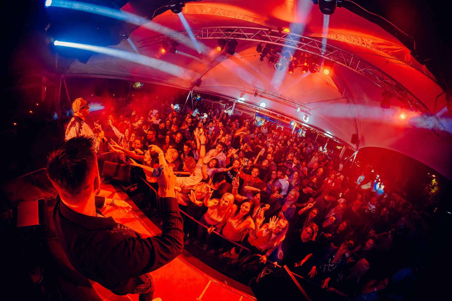 A crowded nightclub dance floor illuminated by red and blue lights creates an energetic party atmosphere.