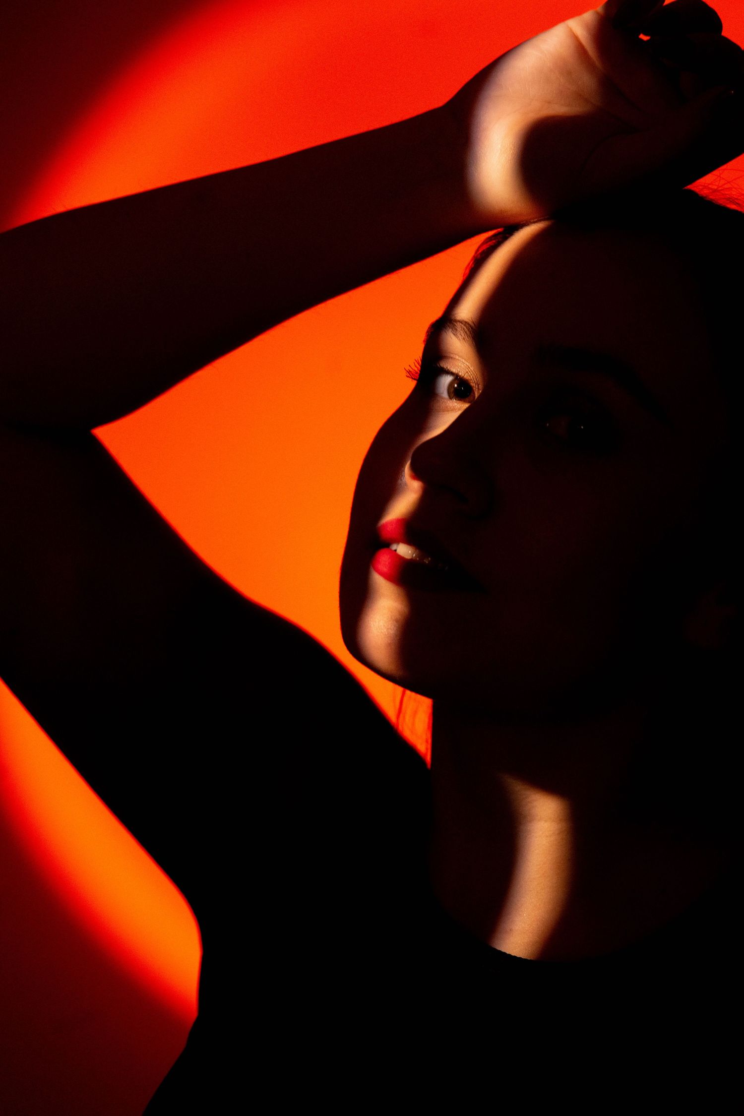 Dramatic portrait in vibrant red lighting showcasing strong shadows and crimson tones against dark background.