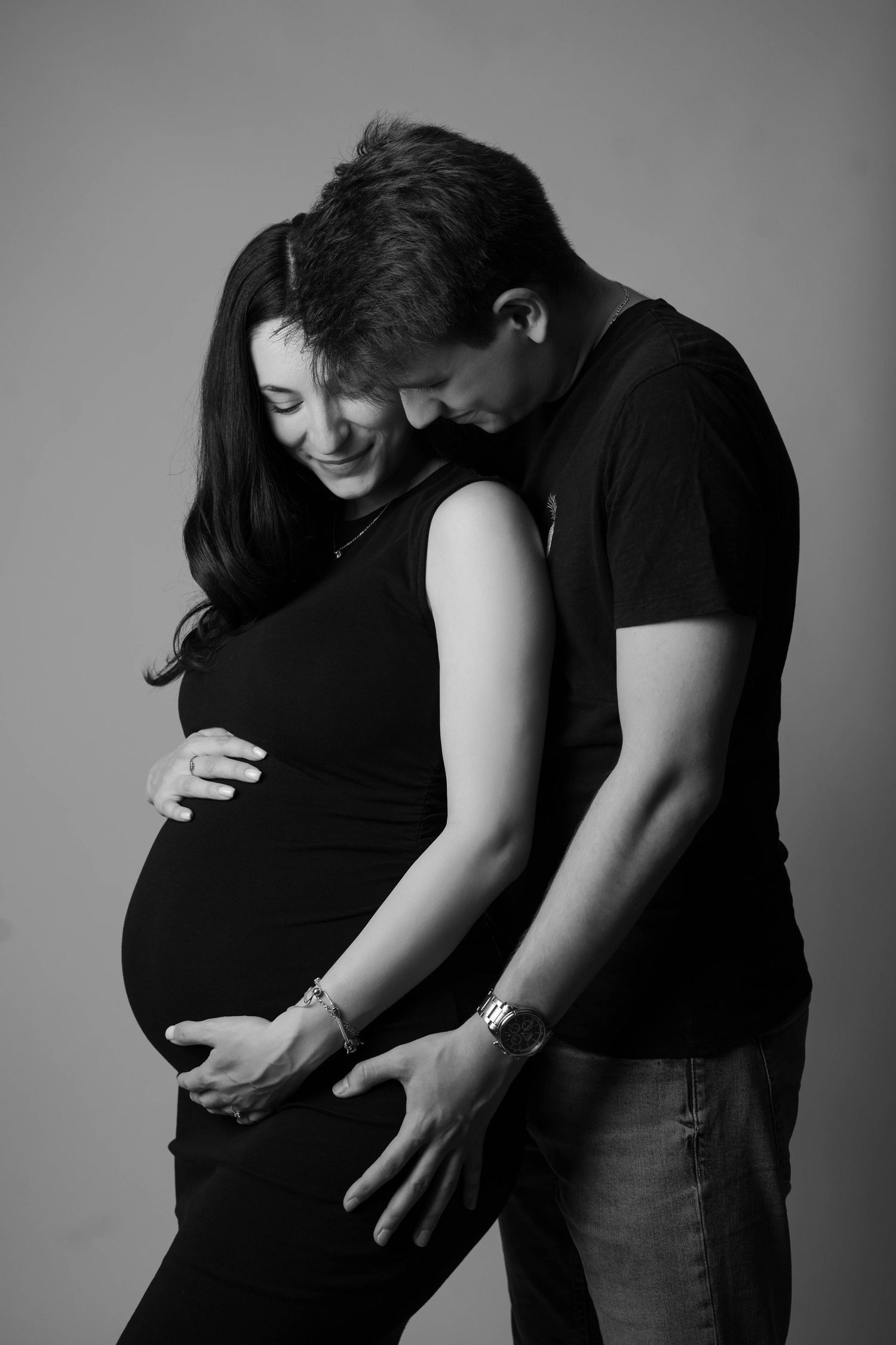 A black and white maternity photo showing an intimate moment between a couple as they embrace the pregnant belly.