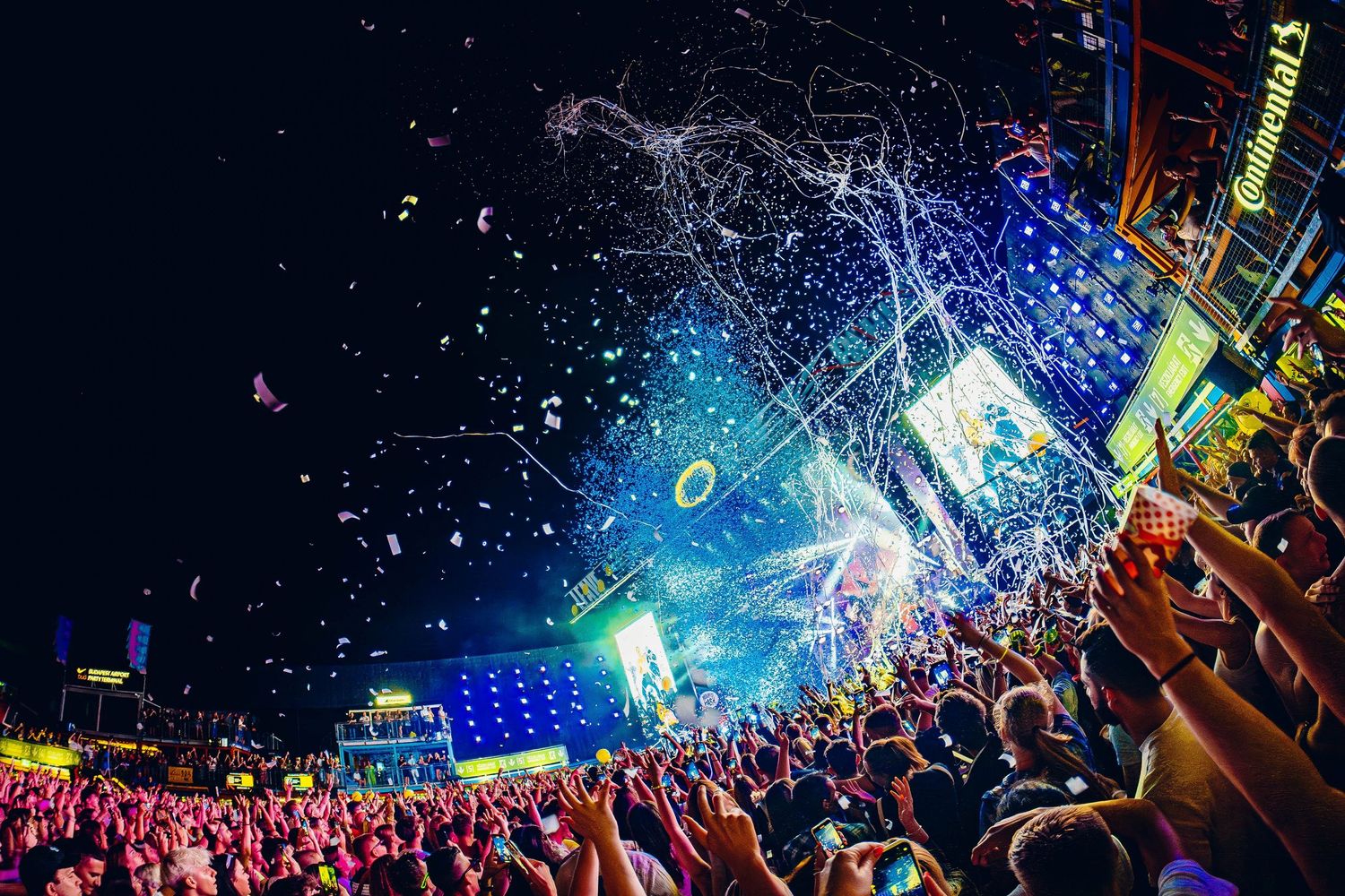 Spectacular light show and water effects illuminate a massive outdoor festival crowd at night.