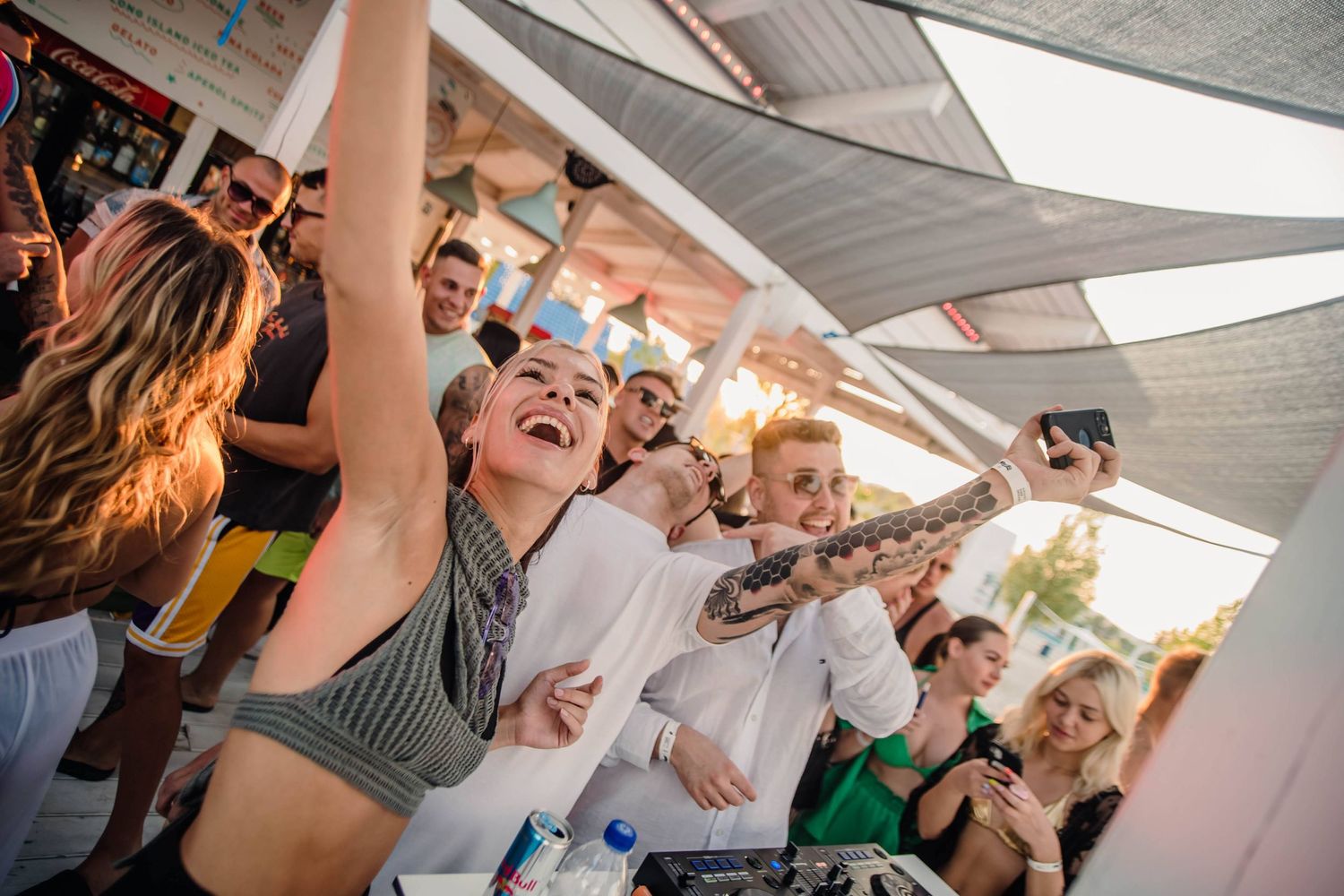 Party-goers dance with raised arms under a covered outdoor venue.