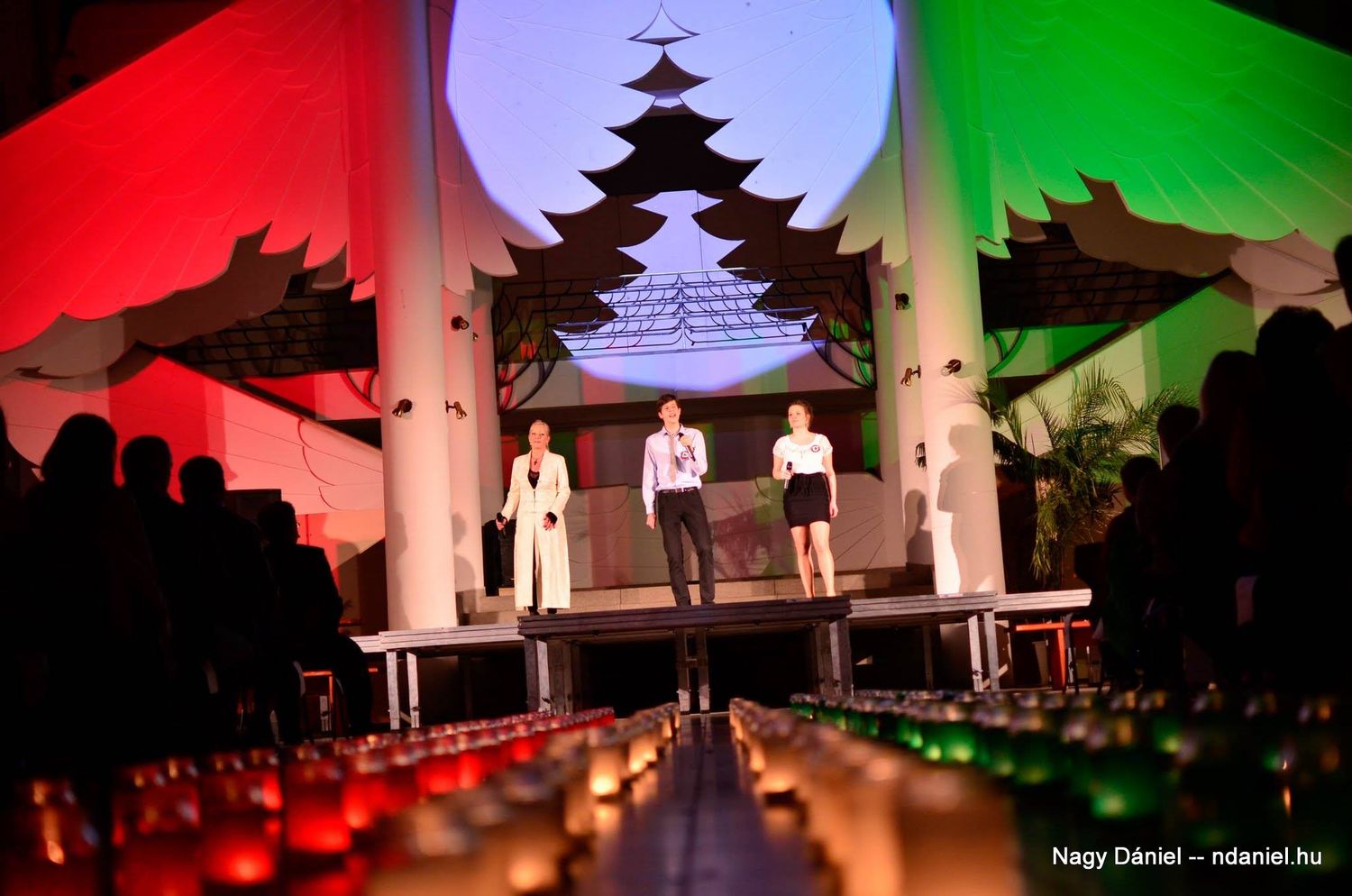 Stage performers stand before a dramatic backdrop with Japanese pagoda silhouette illuminated by red, white and green lighting.