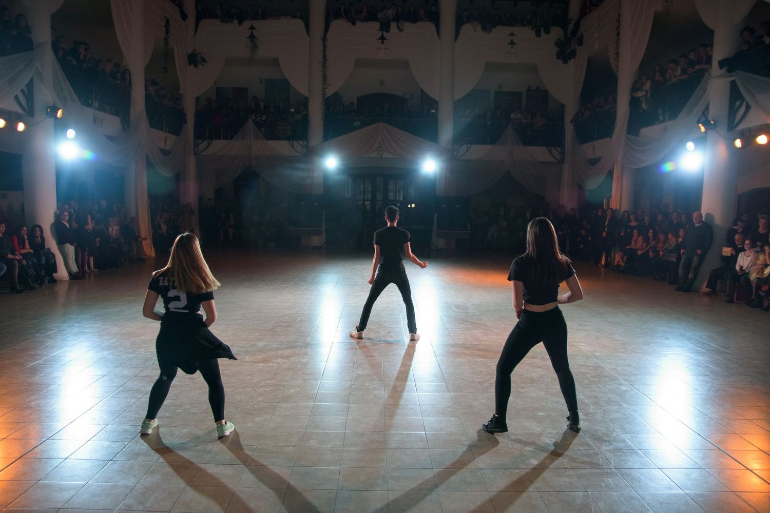 Silhouetted dancers performing on illuminated stage during night performance with audience in background.