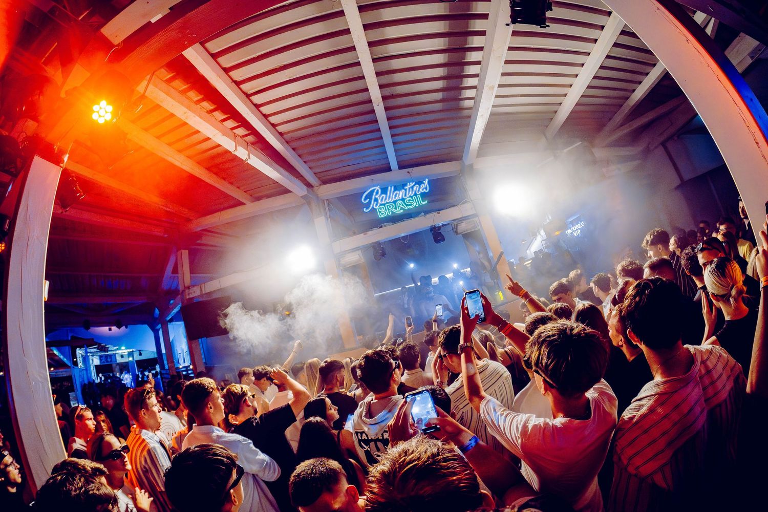 Crowded nightclub dance floor with atmospheric fog, colorful lighting and energetic crowd in party atmosphere.