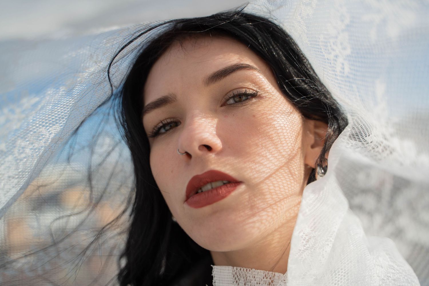 Outdoor portrait with windswept hair against cloudy sky.
