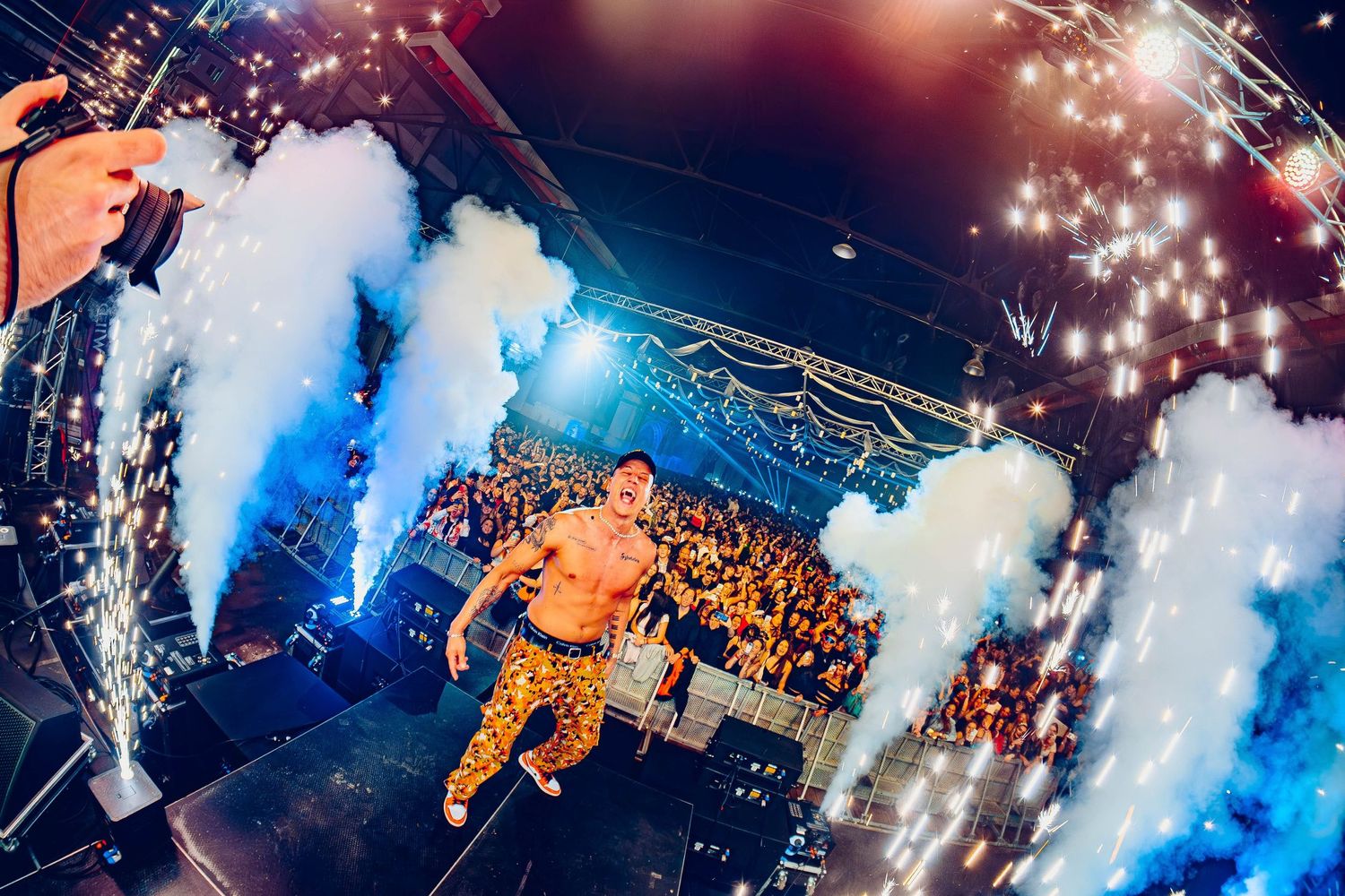 Concert performance with white smoke effects and pyrotechnics illuminating the crowd.