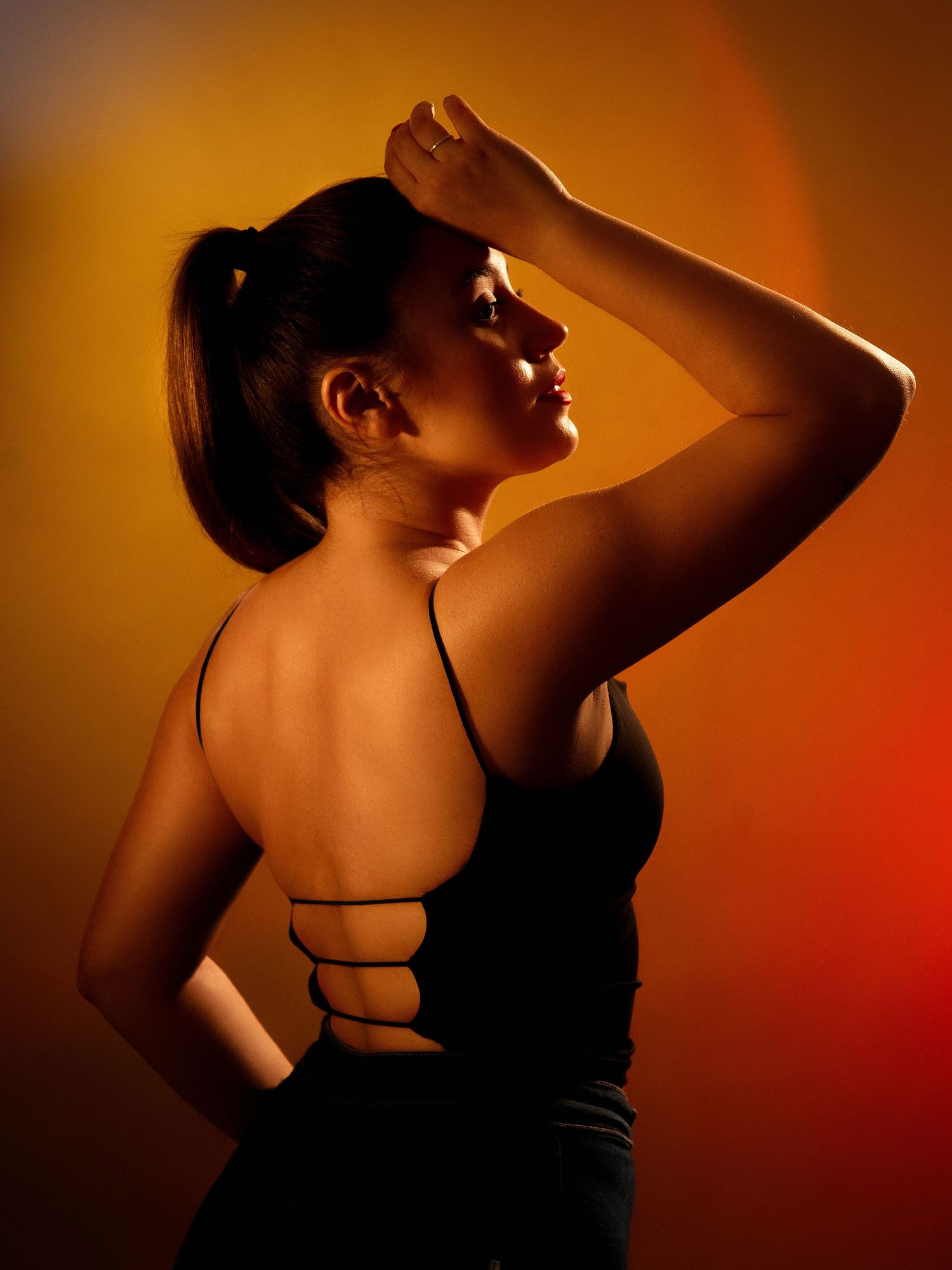 Dramatic silhouetted figure poses against warm orange backdrop in artistic portrait series.
