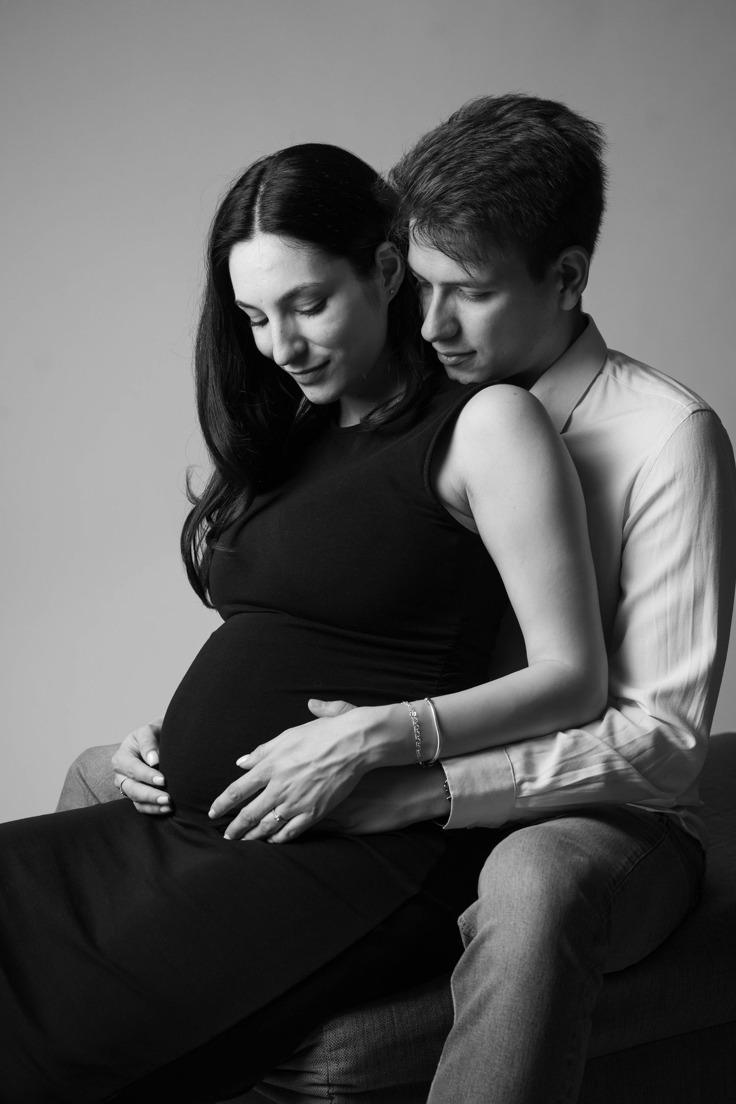 Black and white maternity photo of an intimate moment with a couple sitting together and touching the pregnant belly.