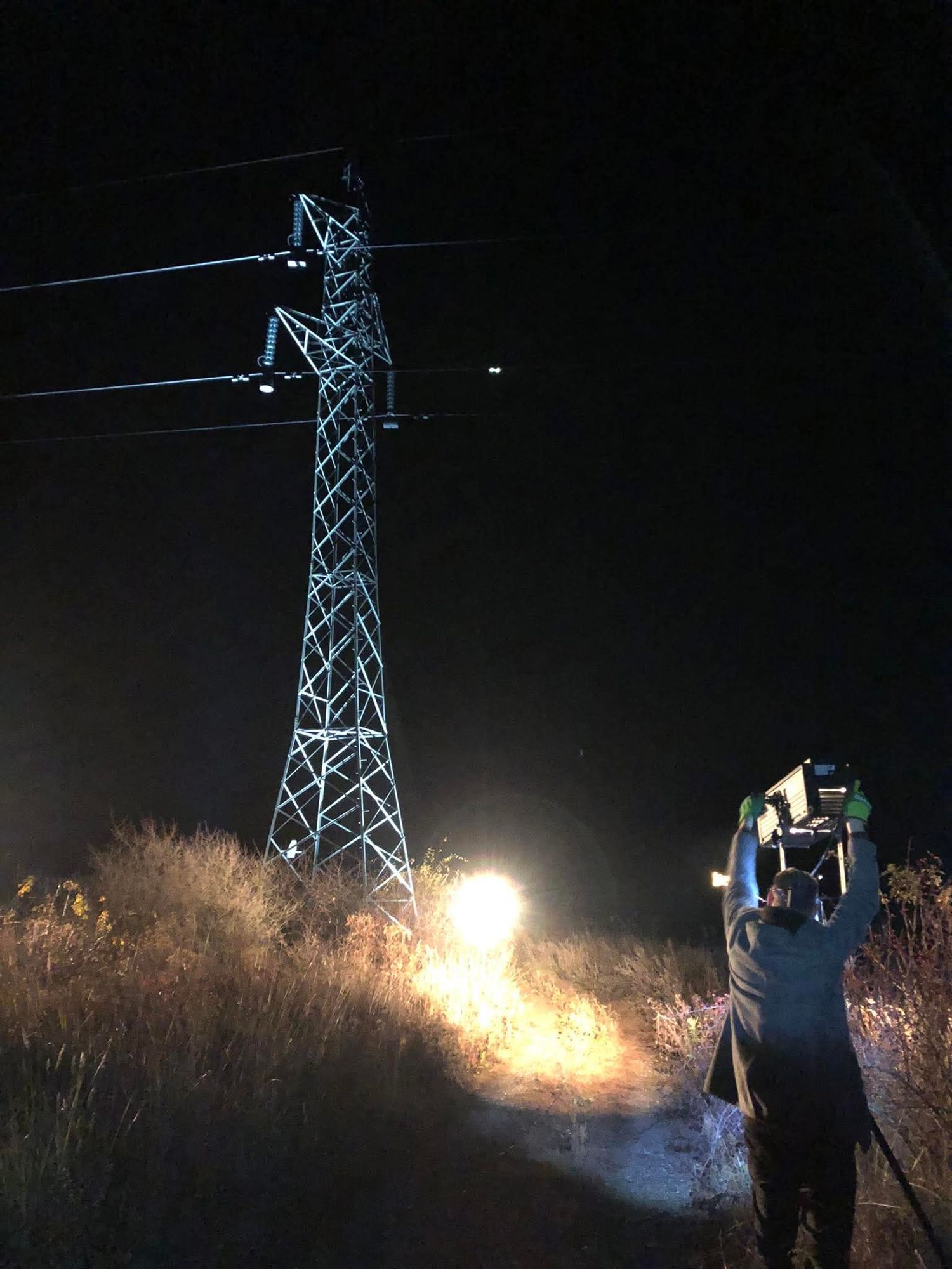 Person with flashlight illuminates electric transmission tower against dark night sky in sequence of progression shots.