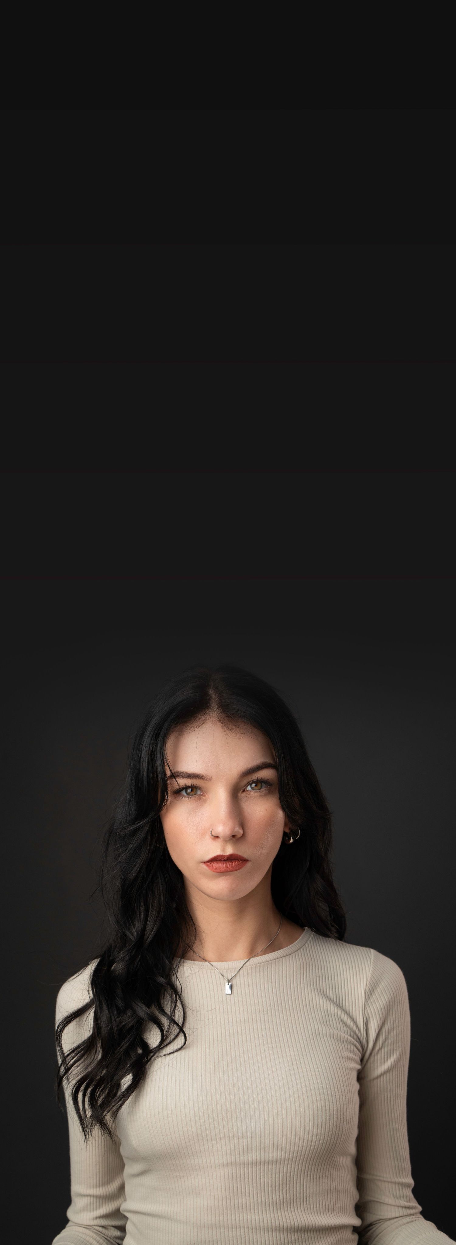 Studio portrait with dramatic lighting featuring a ribbed beige sweater against dark background.