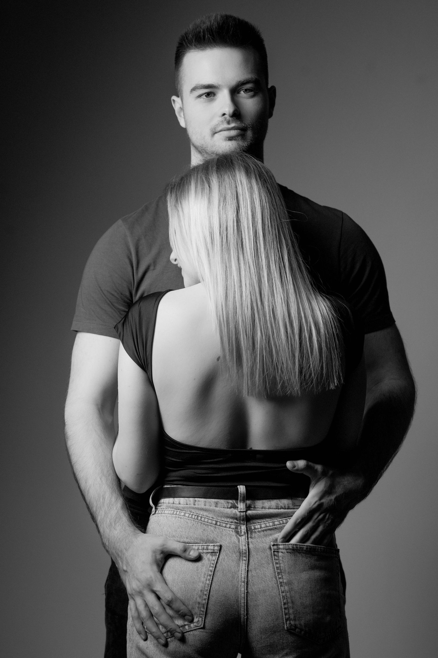 Black and white artistic portrait of intimate couple embracing, with focus on blonde hair against dark shirt.