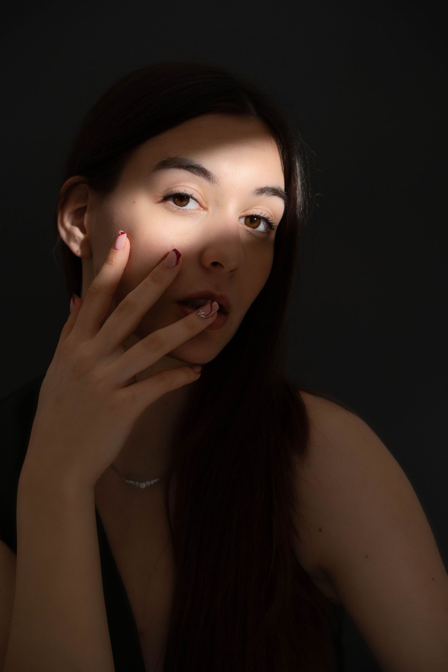 Artistic portrait with dramatic lighting and hand gesture against dark background.