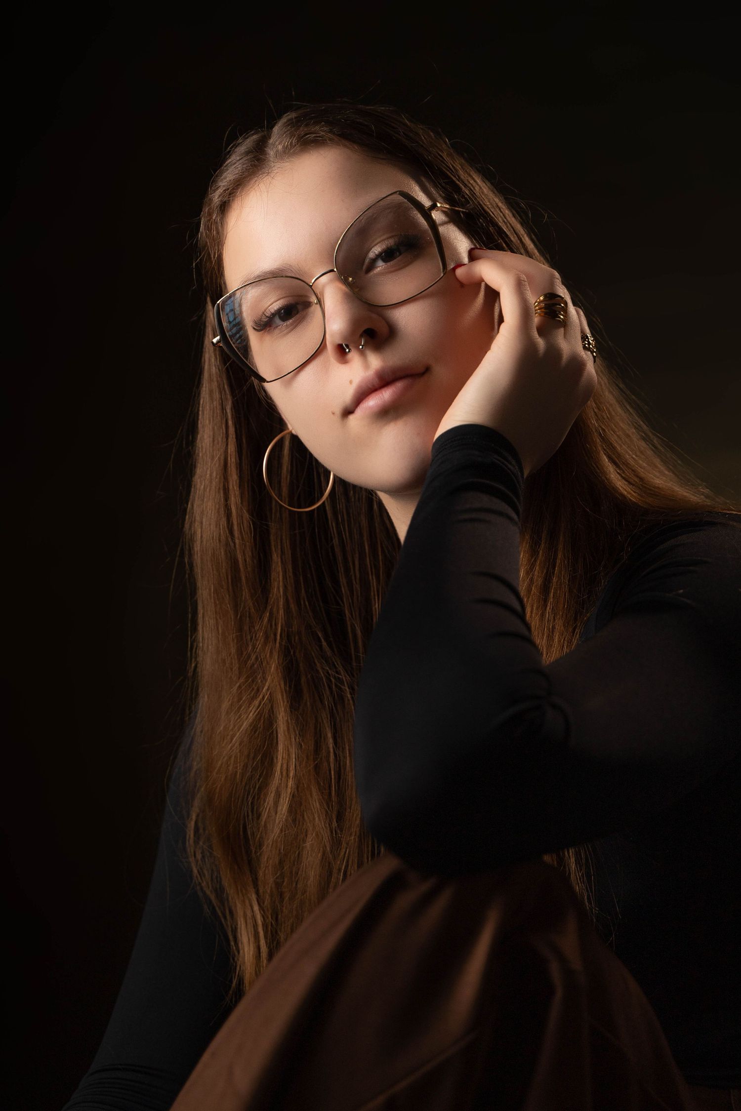 Elegant portrait with glasses and hoop earrings in moody lighting.