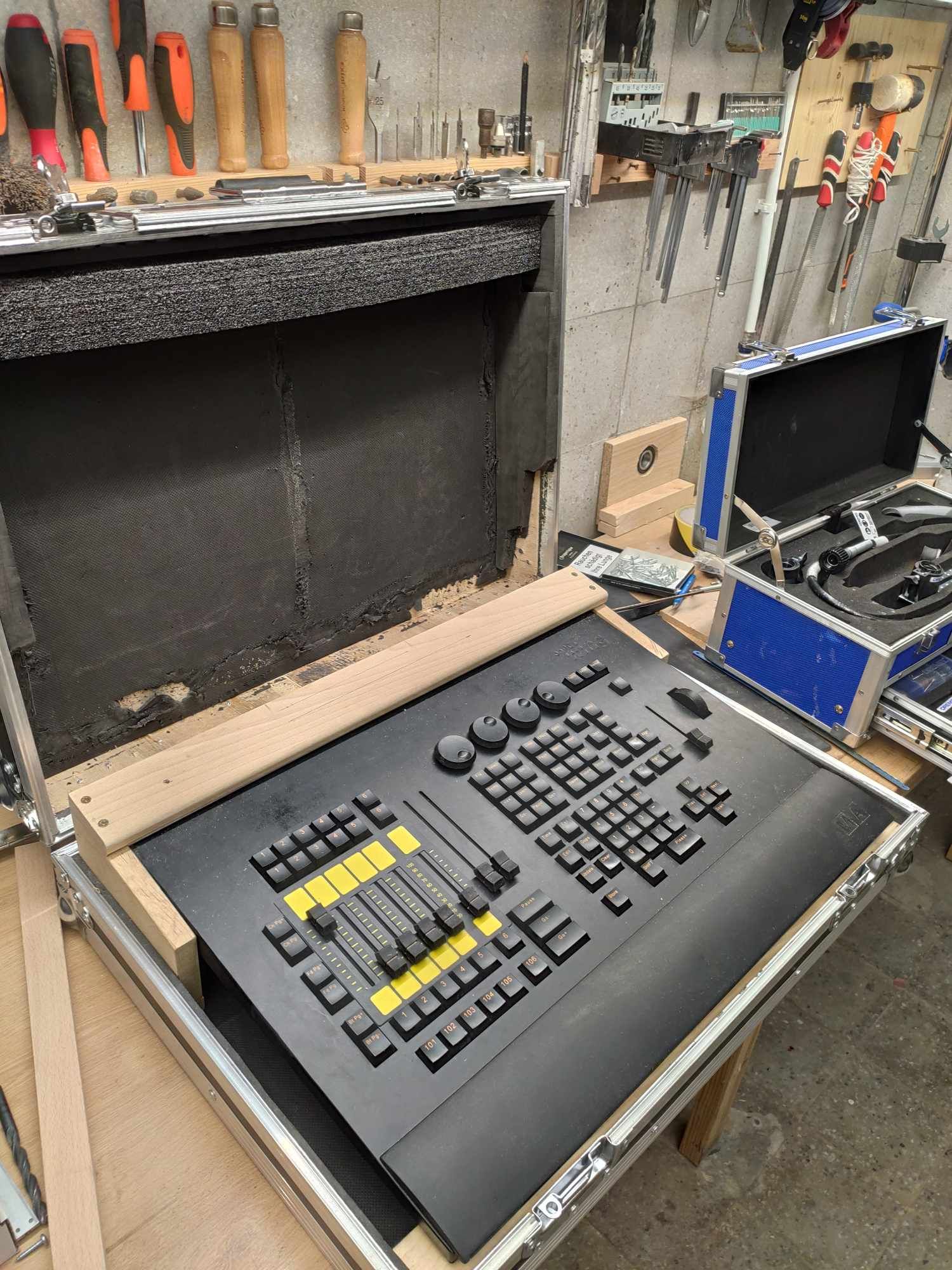 Professional lighting control board in road case with faders and buttons on workbench with tools hanging in background.