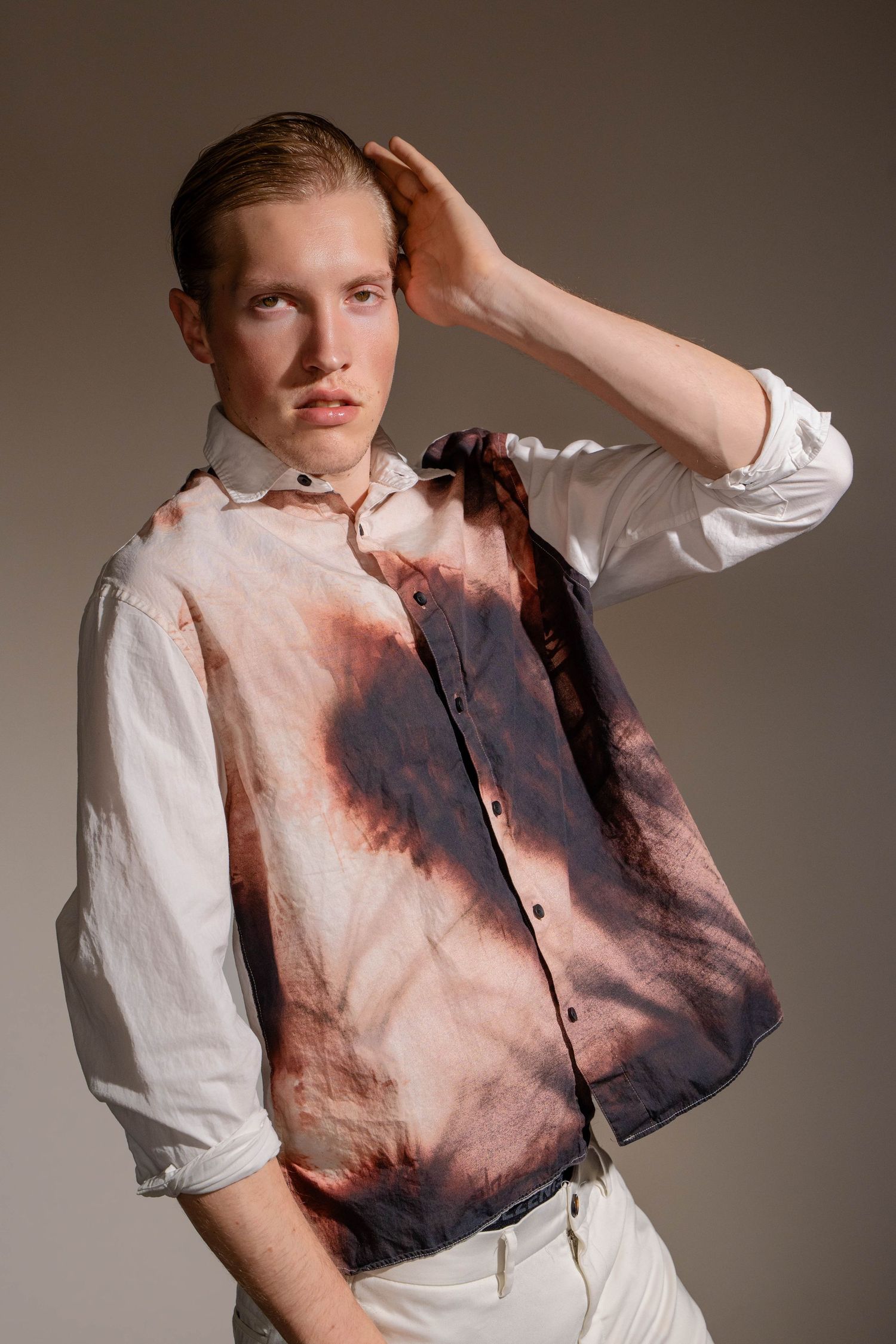 Fashion portrait with tie-dye effect white shirt featuring pink and dark stains against neutral studio background.