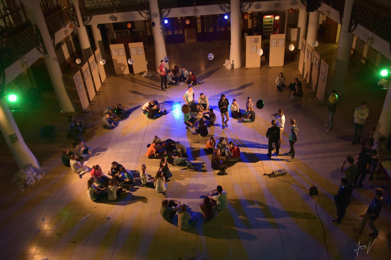 People relax on bean bags in an illuminated indoor space with colorful lighting and tall columns.
