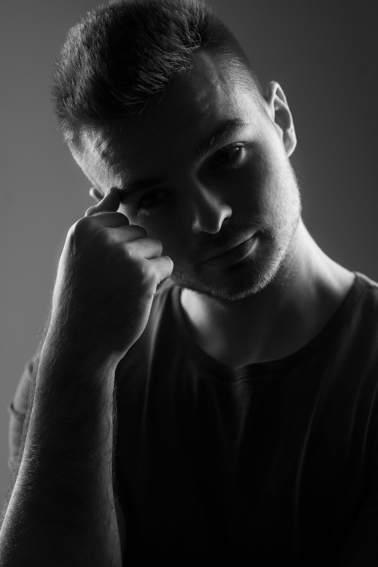 Black and white dramatic portrait with moody lighting highlighting thoughtful expression and shadow play.