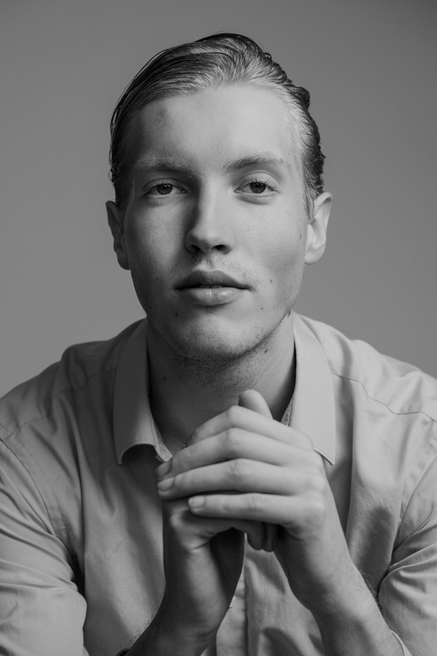 Black and white portrait of a young person in a light colored shirt with clasped hands and thoughtful expression.