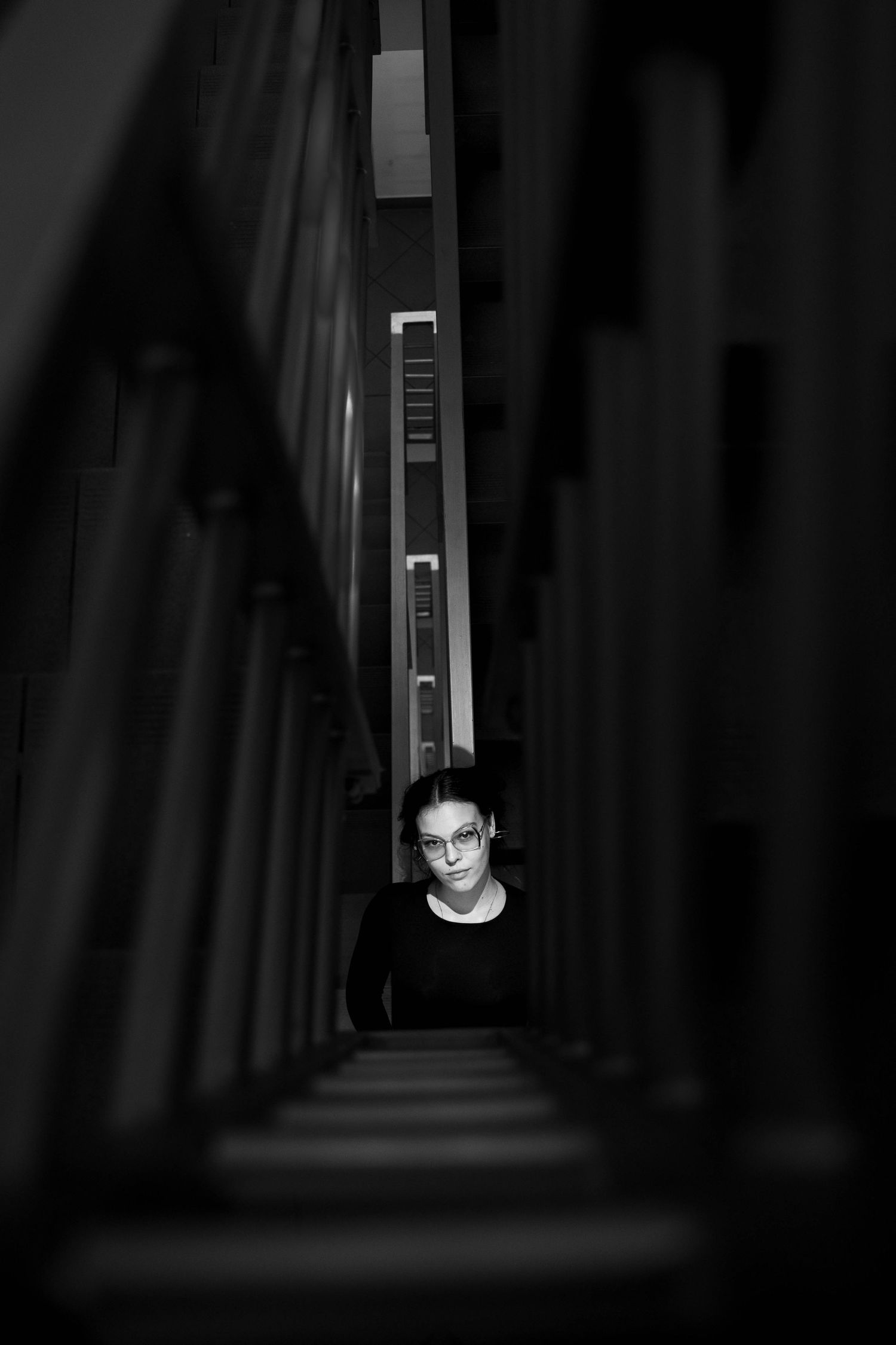 Dramatic black and white portrait of someone in a narrow architectural space with strong vertical lines.