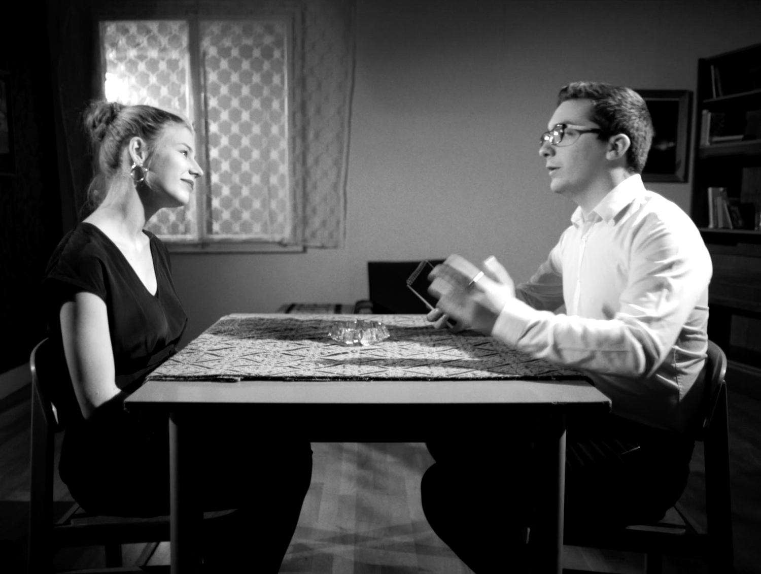 A black and white photo of two people engaged in an animated discussion at a table.