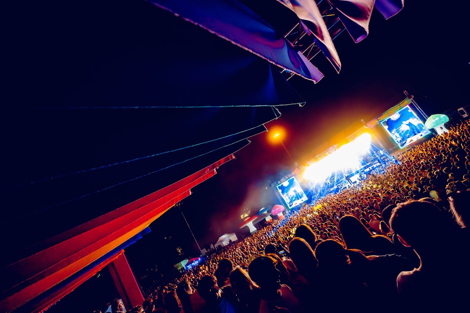 Concert arena viewed from above with red lighting and electronic displays illuminating the massive crowd.