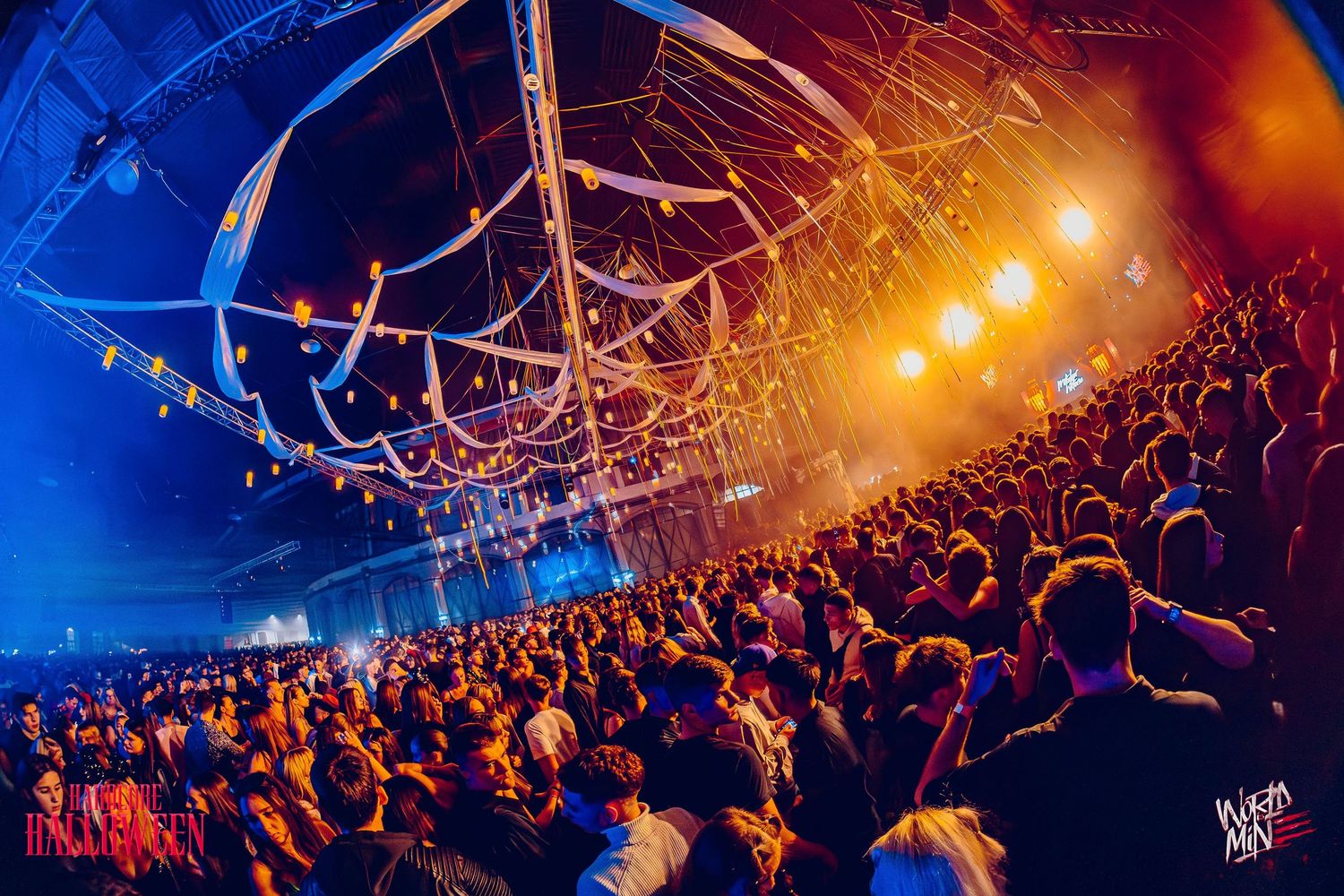 Crowded concert venue with overhead lighting and audience stretching into the distance.