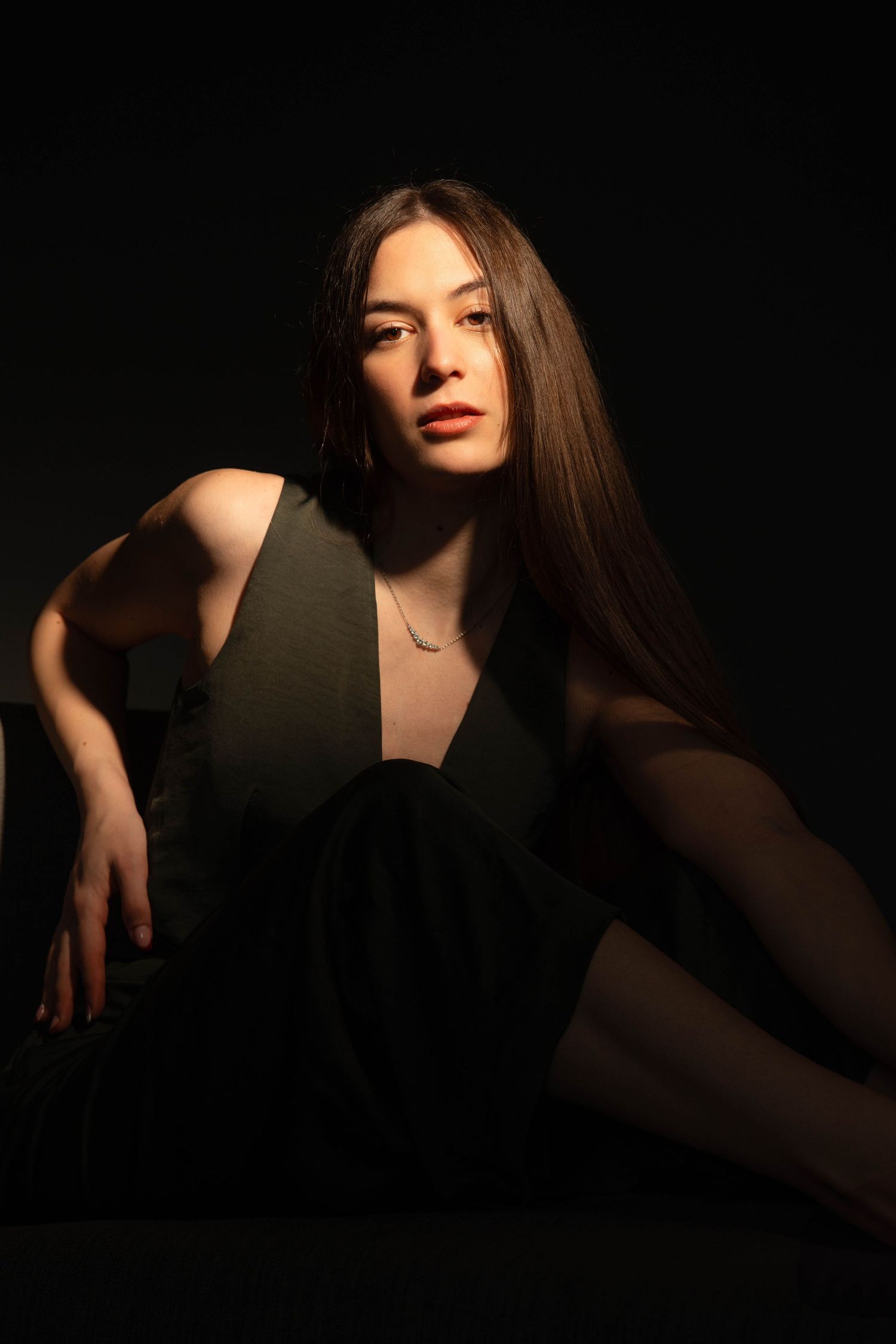Fashion portrait with dramatic side lighting and black dress against dark background.