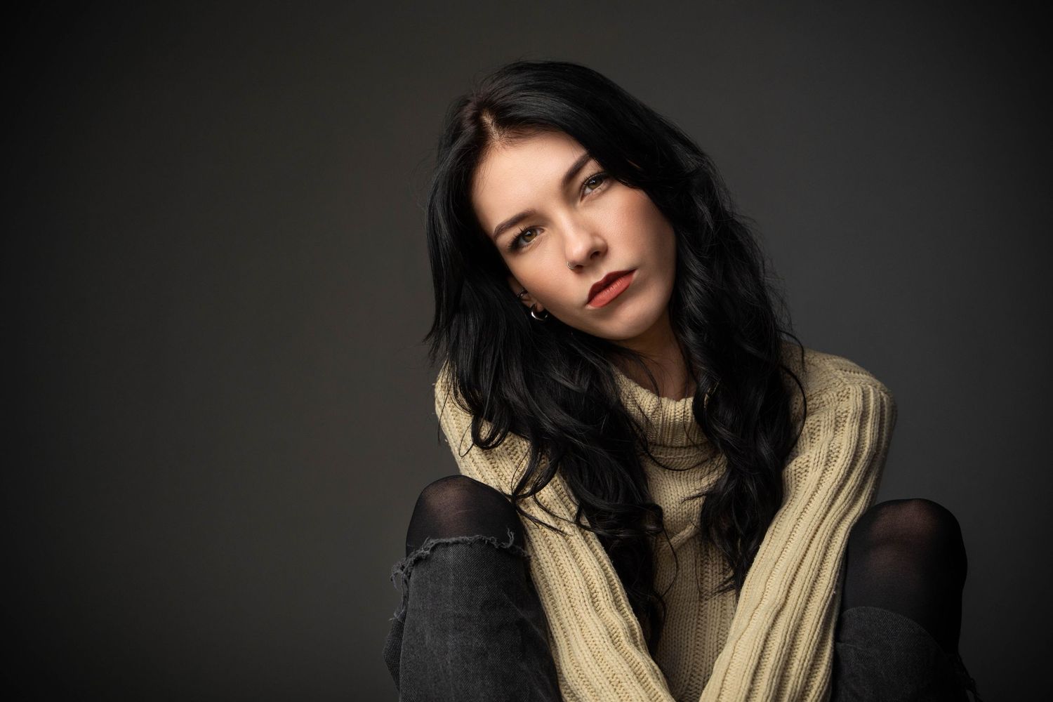 Dramatic studio portrait in cream turtleneck sweater against dark background.