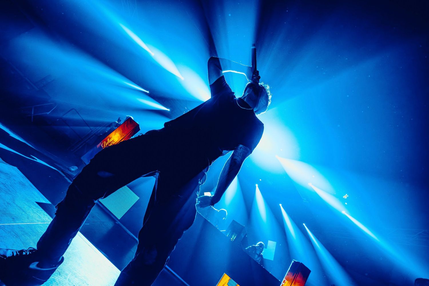 Silhouetted concert performer against bright blue stage lights creating dramatic beams.