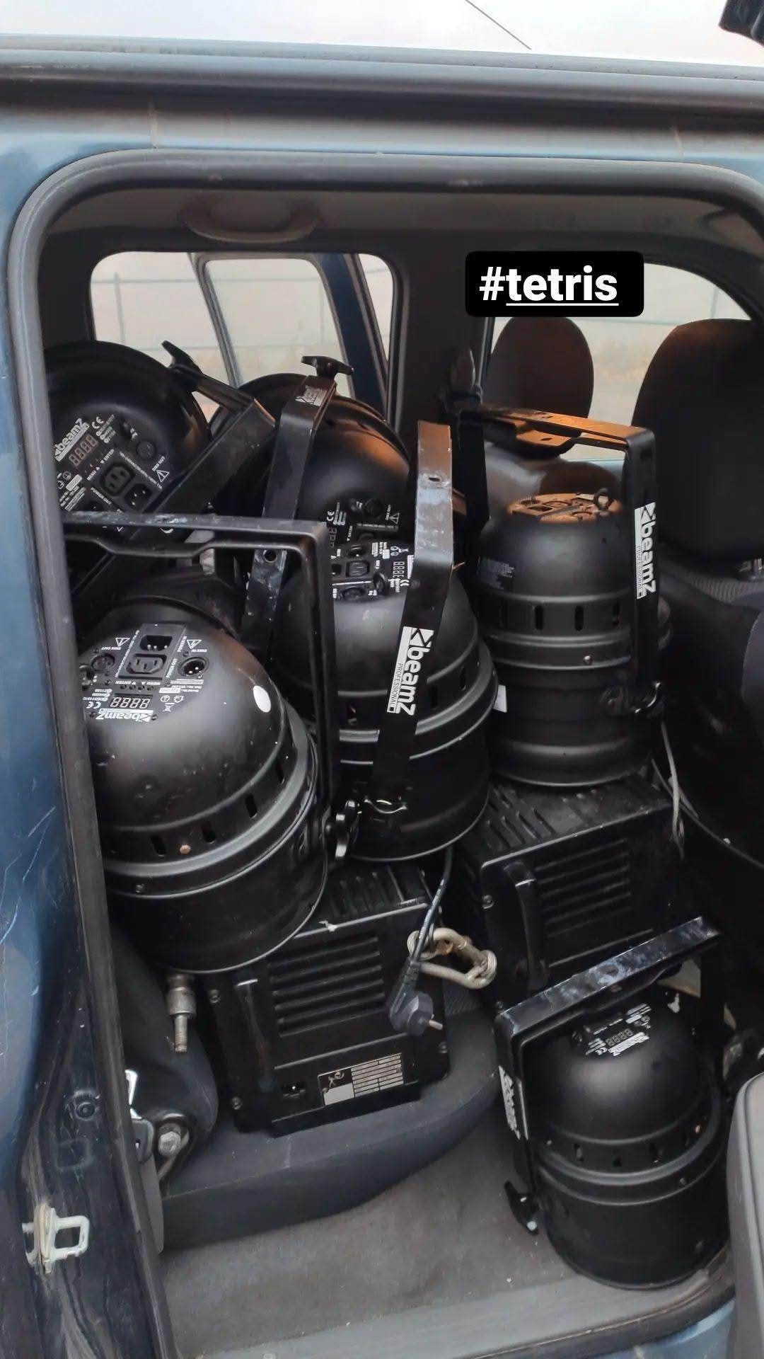 Multiple black Tetris LED stage lighting fixtures are arranged in the back seat of a vehicle's interior.