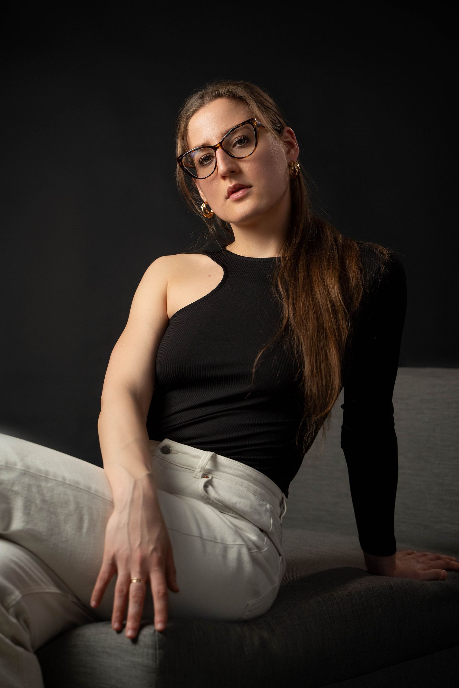 Studio portrait with dramatic lighting of woman in black top and white pants.