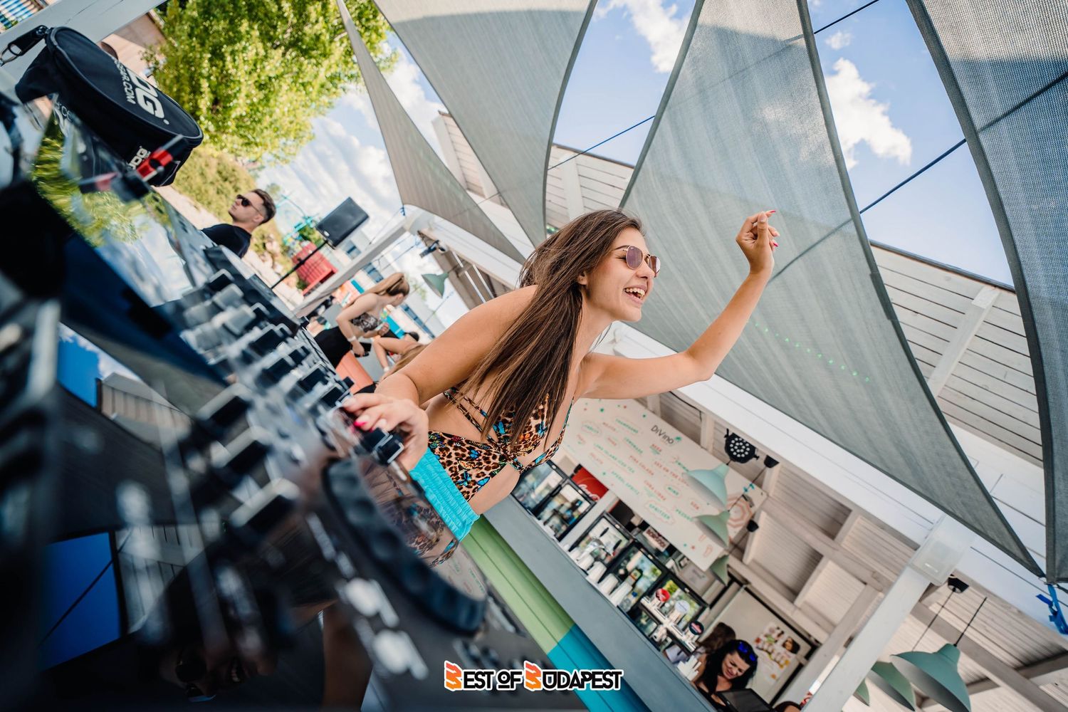 A dancer performs energetically at an outdoor event with modern architecture in the background.