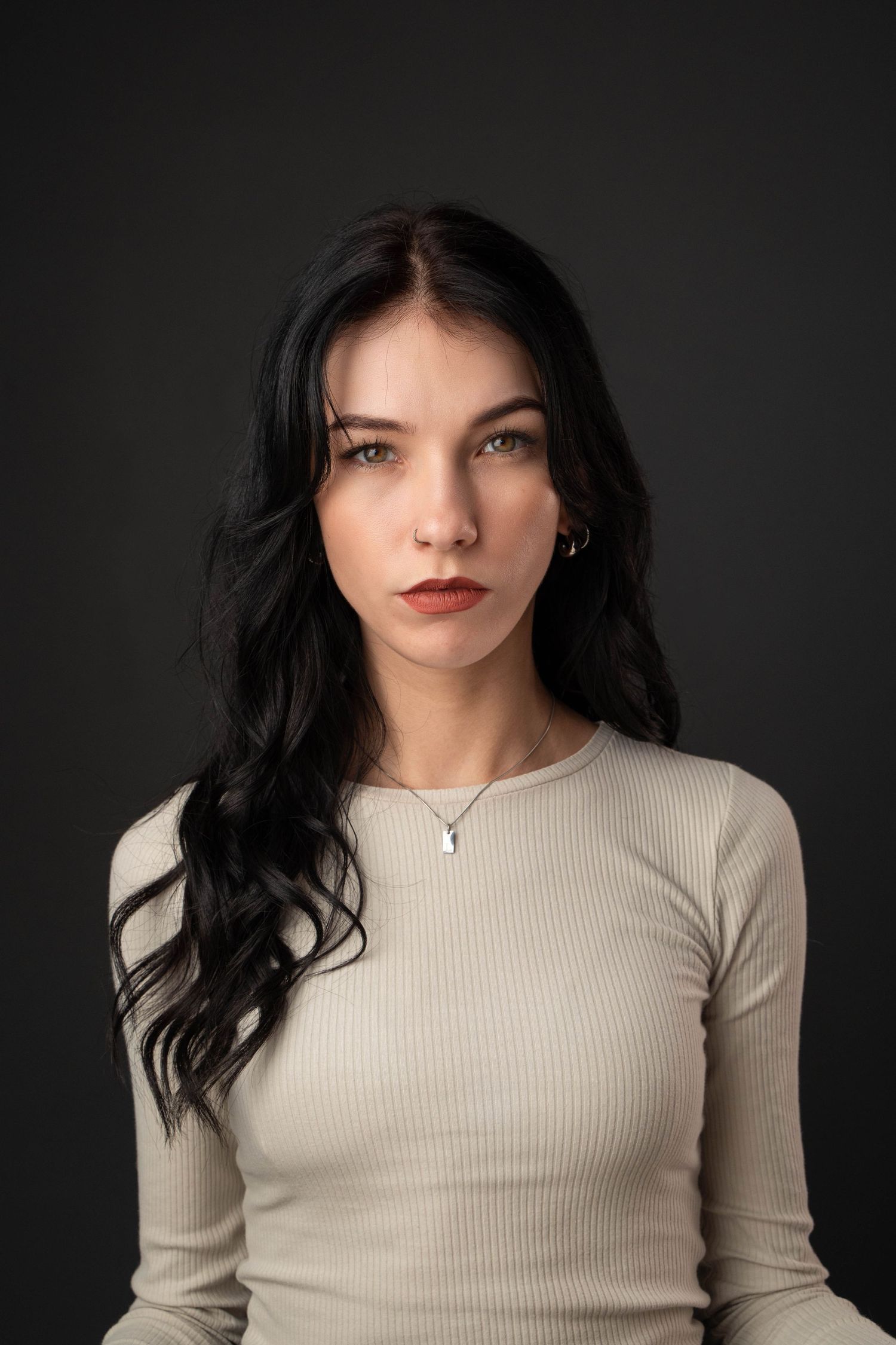 Portrait in cream ribbed top with long dark hair against grey background.