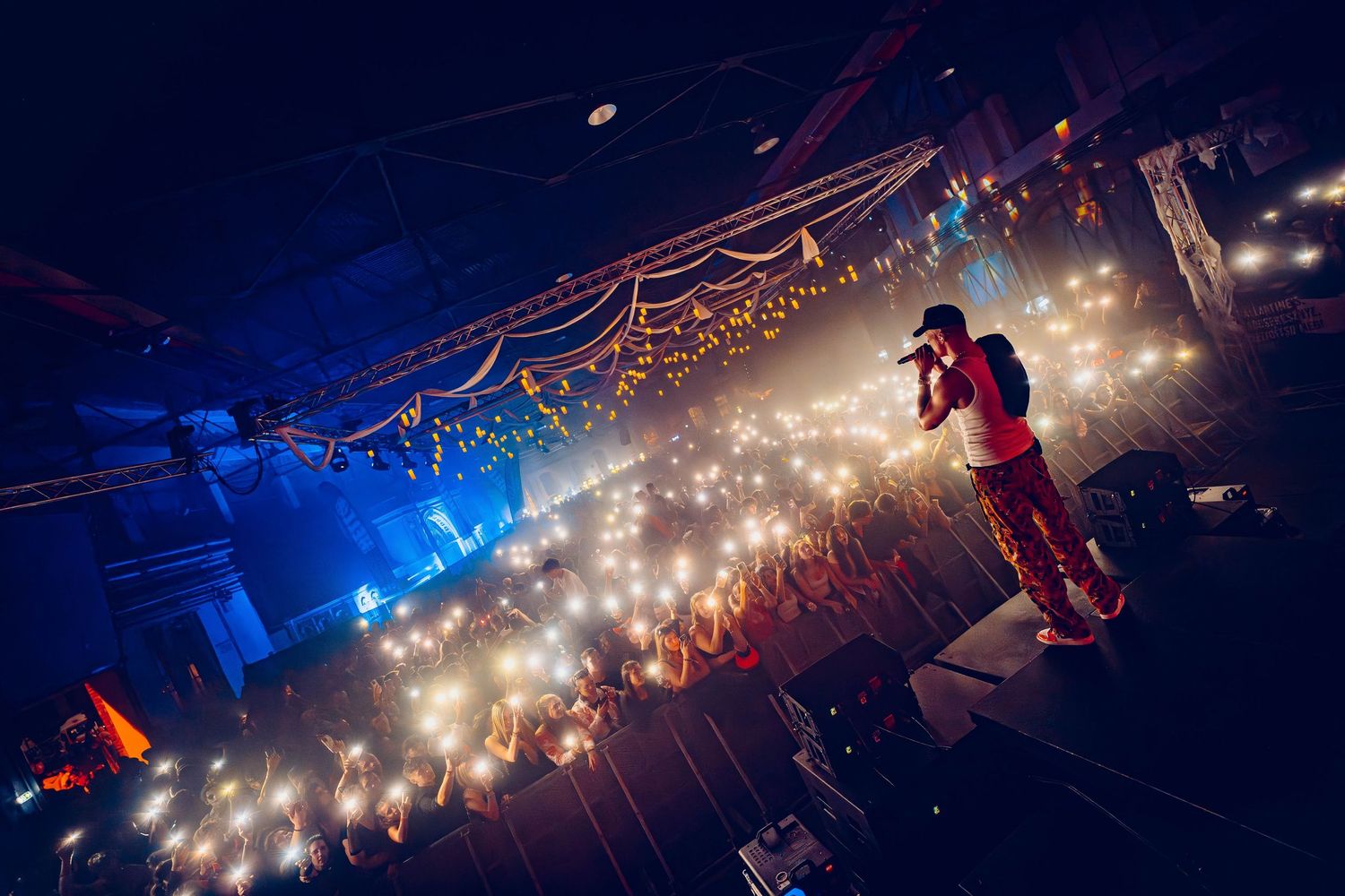 Performer silhouetted on stage with a sea of glowing phone lights in the audience.