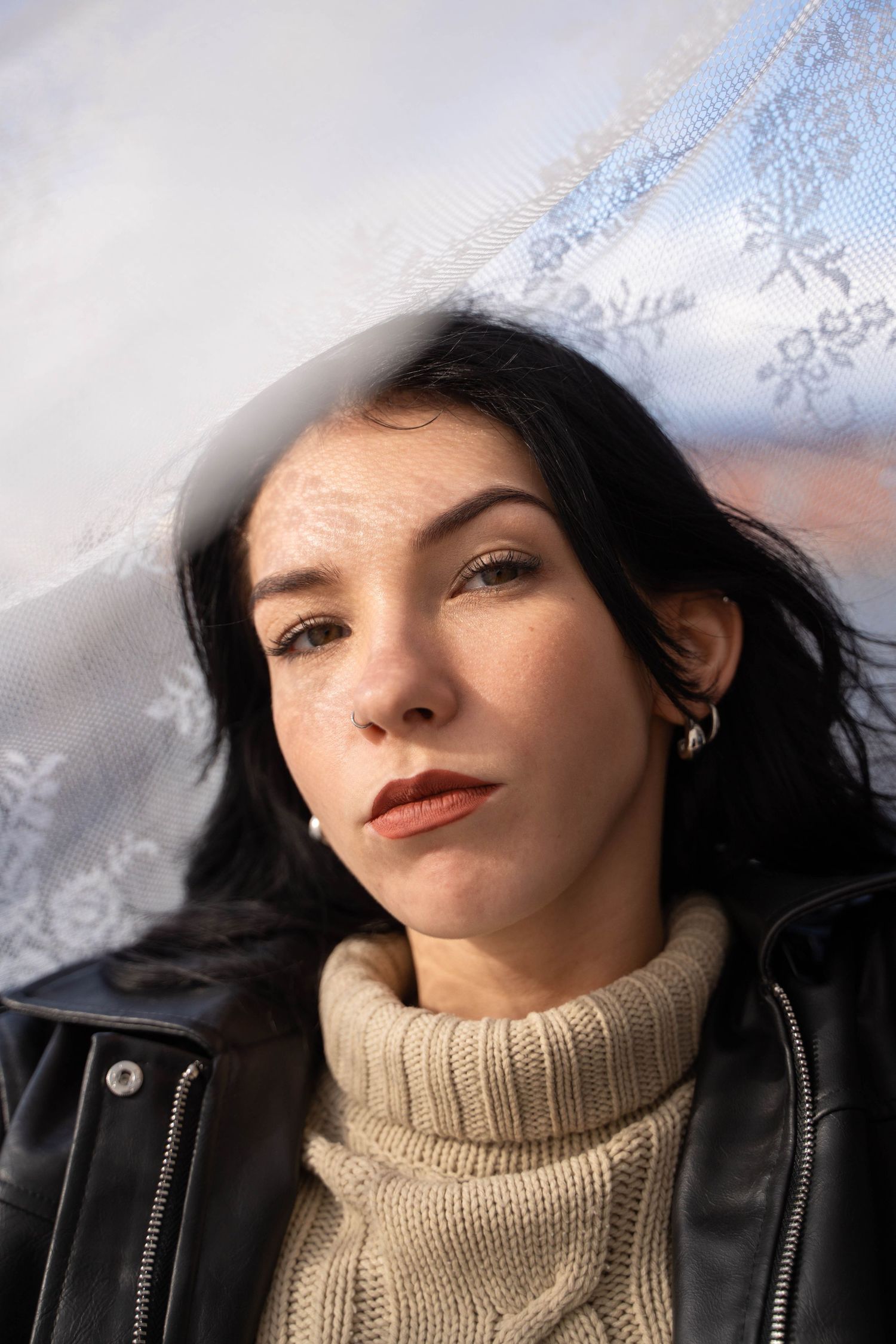 Fashion portrait with dark hair wearing cream turtleneck sweater and leather jacket against snowy background.