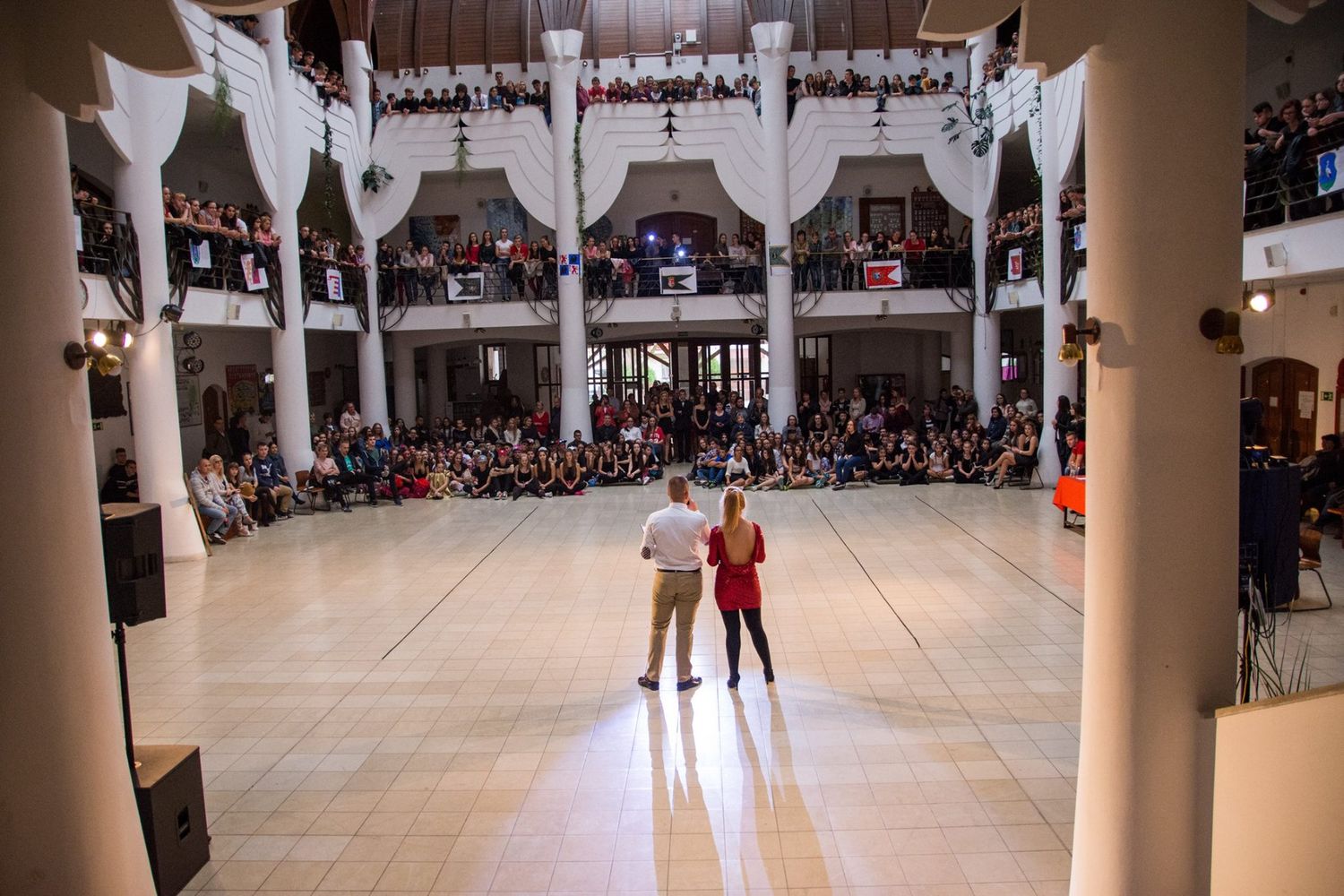 A large indoor gymnasium filled with spectators watching a basketball game from bleacher seats during a sports event.