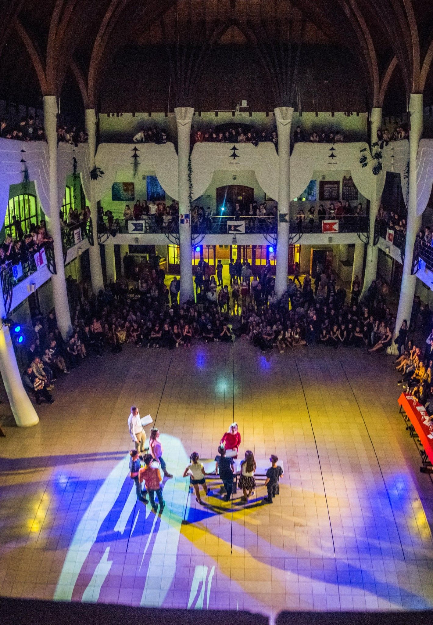 People perform in a dance showcase on a brightly lit stage with colorful spotlights and a large audience watching.