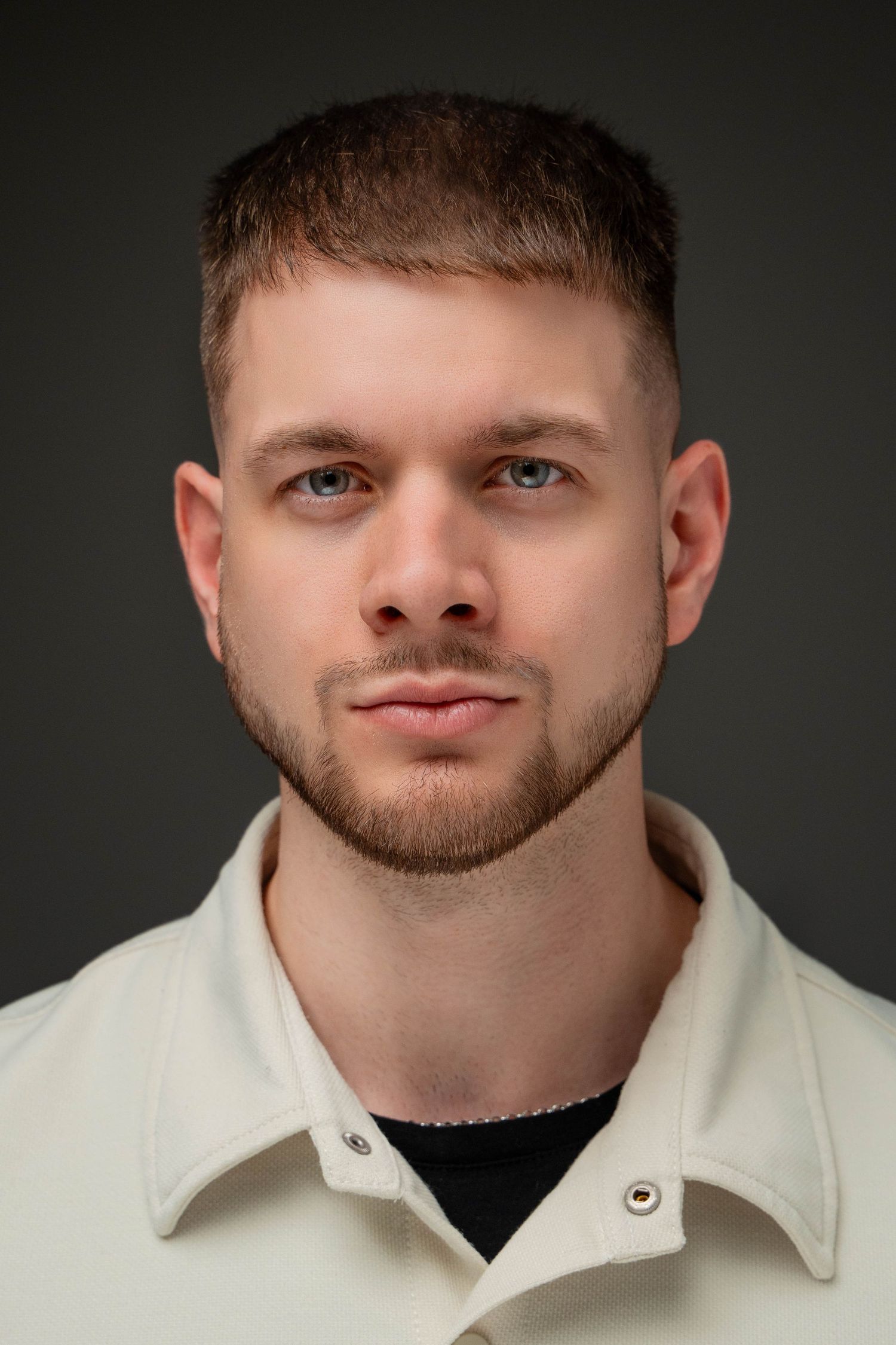 Professional portrait against dark background of person wearing white collared jacket and black shirt.