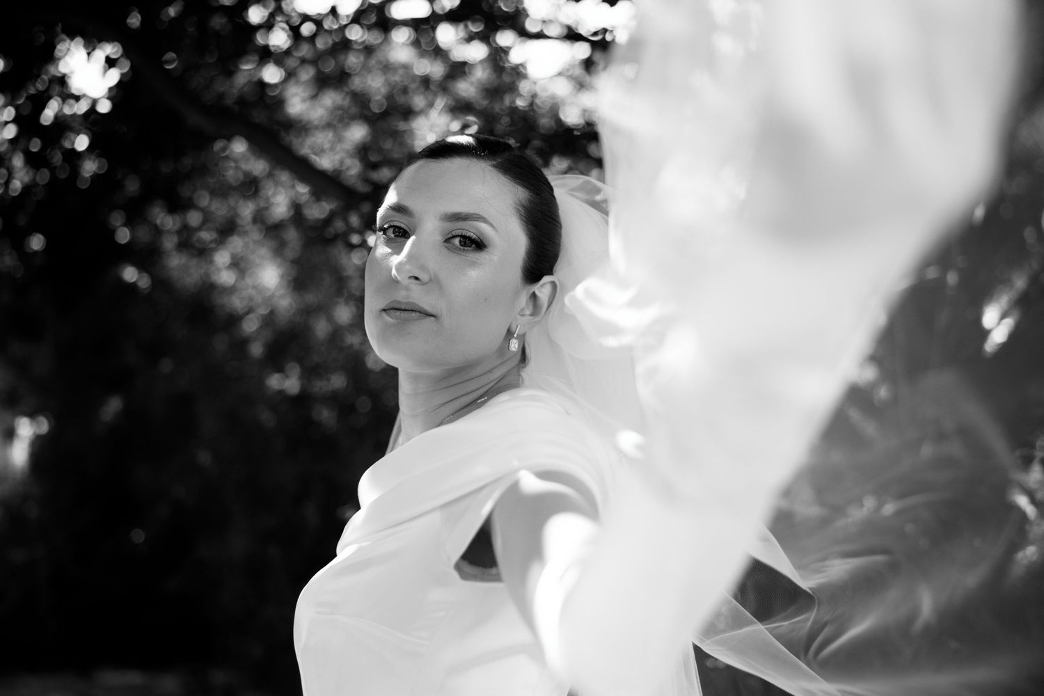 Artistic black and white portrait of bride in sleek white gown with dramatic lighting outdoors.